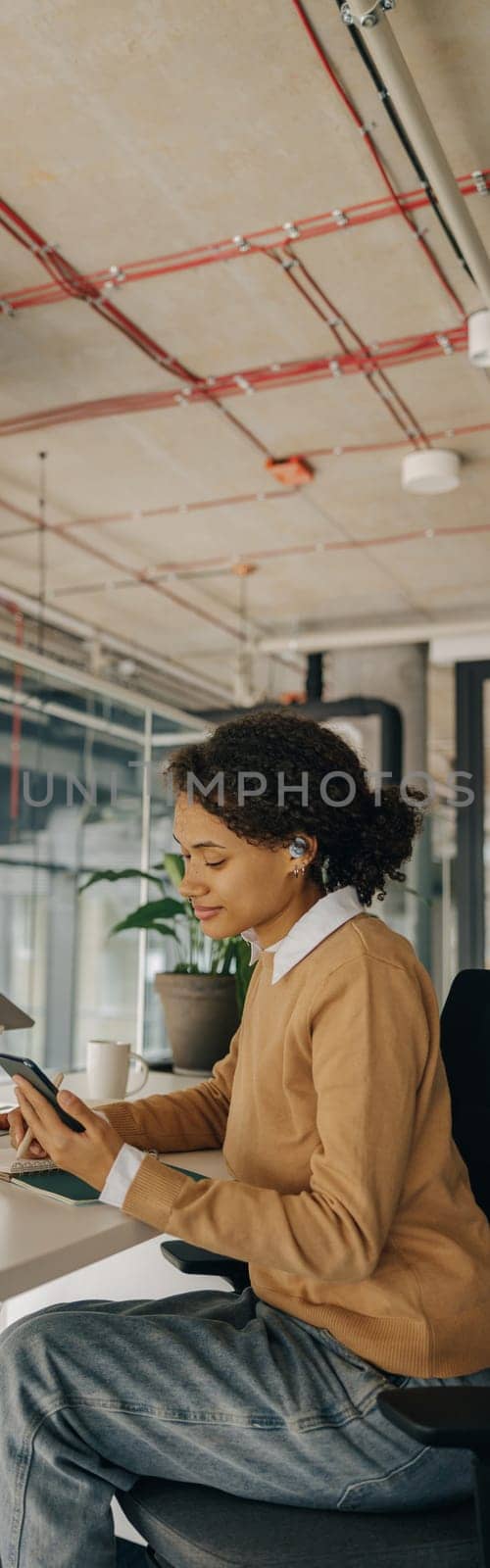 Female freelancer have video conference with client and looking on phone while sitting in coworking