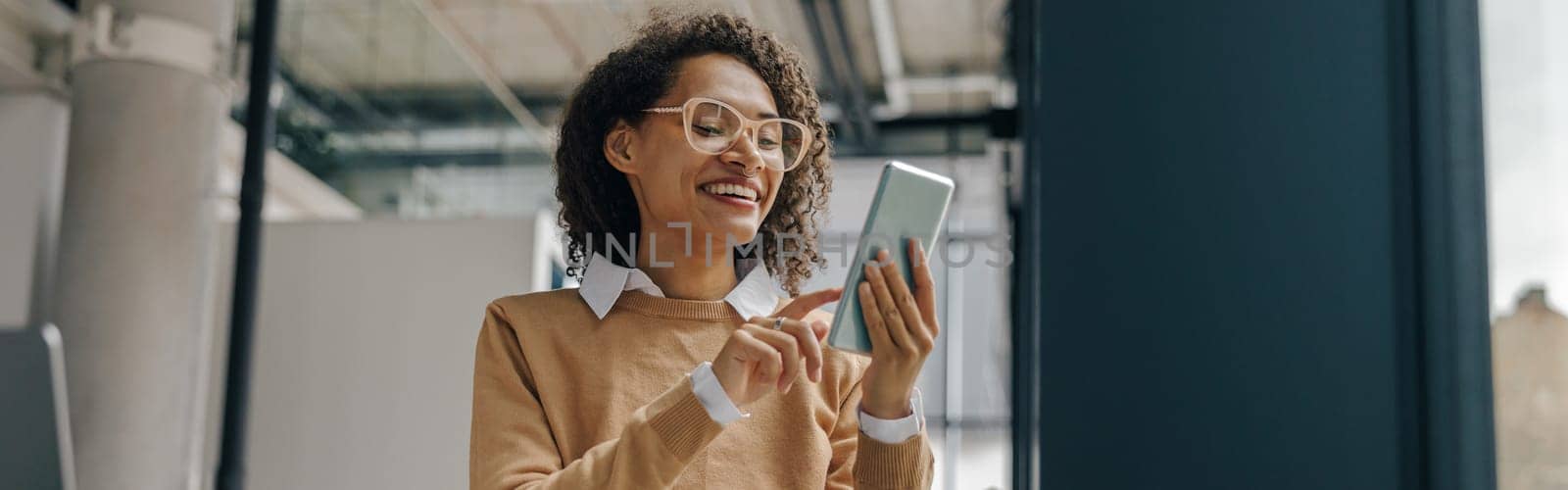 Smiling woman executive manager is using mobile phone sitting in office during break time