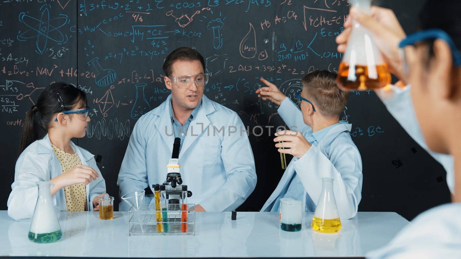 Smart teacher explain about chemical theory while student mixing colored solution or doing experiment. Instructor teaching chemistry while pointing at blackboard in STEM science class. Edification.