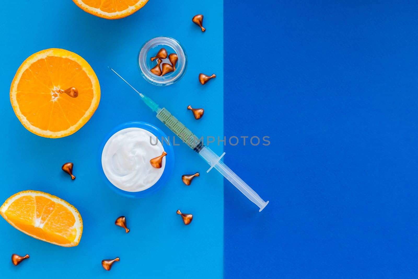 Vitamin C, natural anti aging cosmetics serum and syringe with ornge fruit slices.Cream with oranges on blue background.Natural cosmetics concept.atural beauty product concept.Copy space by YuliaYaspe1979