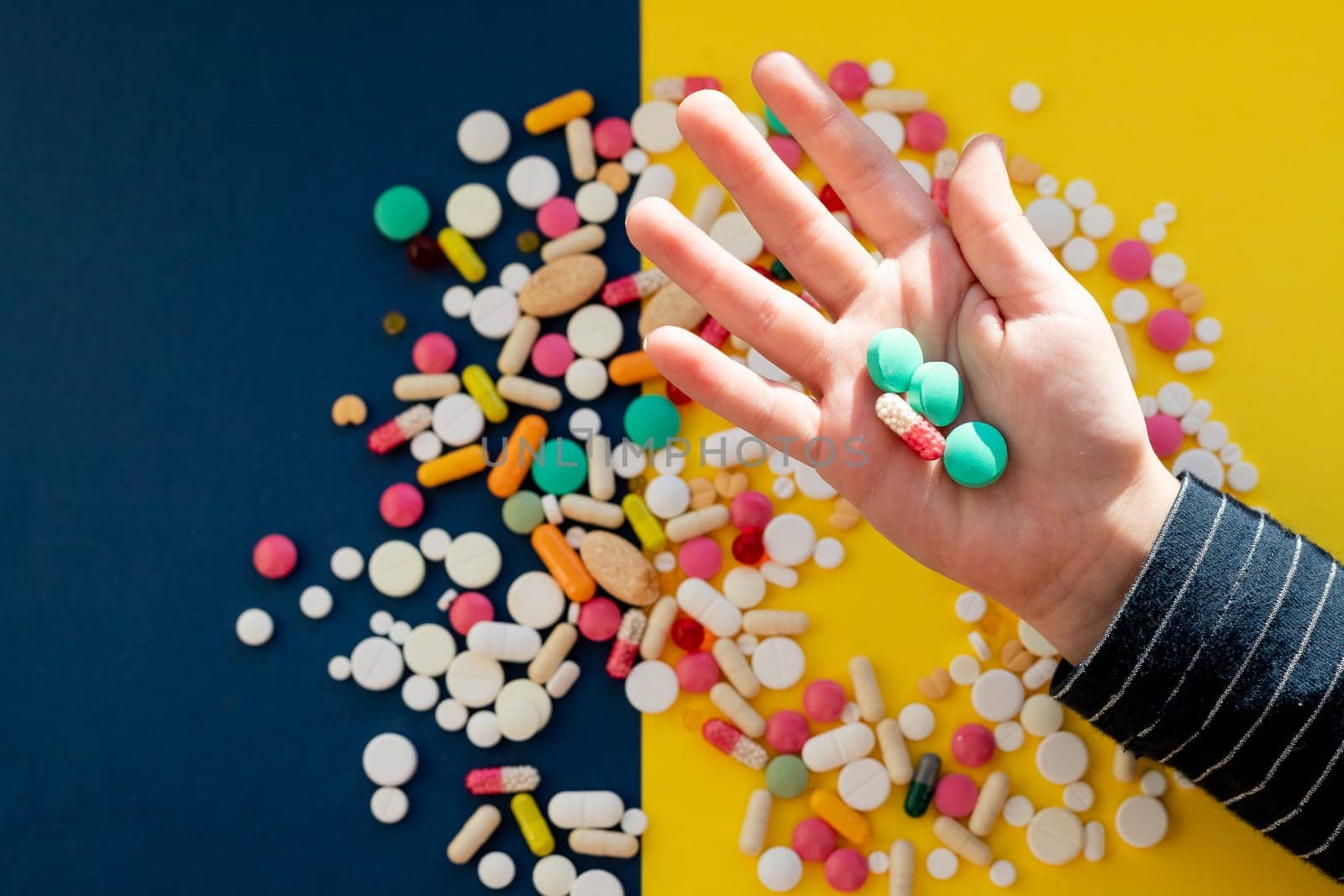 Top view of child hand holding tablet pills against yellow background. Many tablets, pills, medicines
