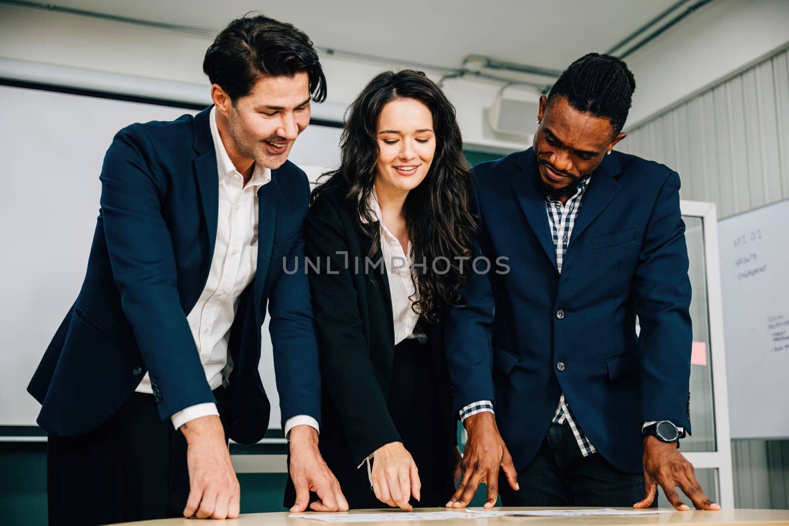 At a conference room desk, business colleagues stand, actively discussing and planning. Teamwork, diversity, and leadership are evident in this successful gathering. by Sorapop