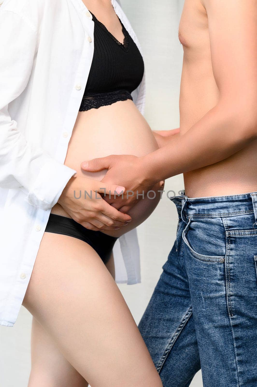 Bare belly of a pregnant woman, a married couple is waiting for the birth of their child, hands on the belly of a pregnant woman.