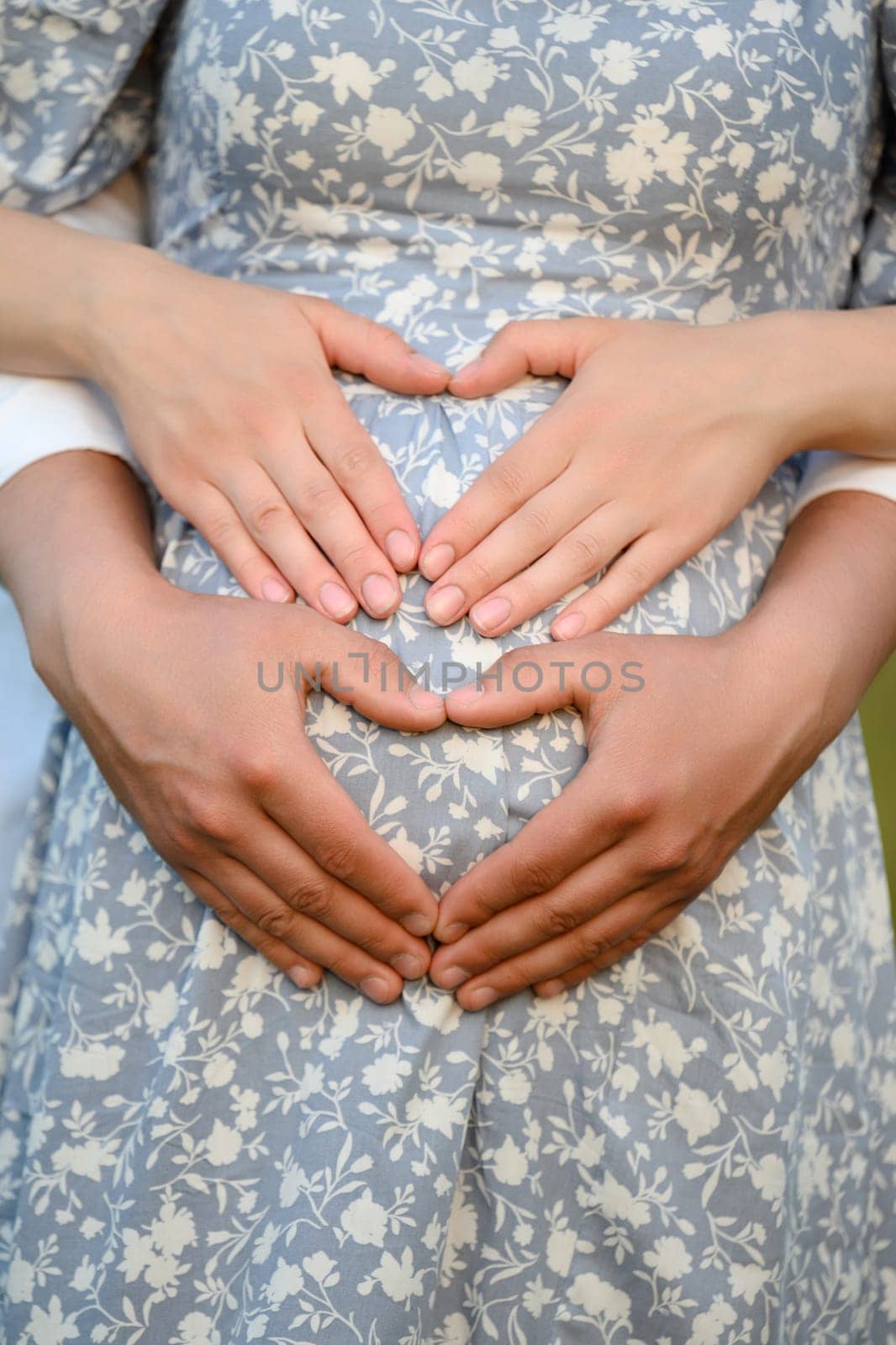 A family couple hugs a pregnant woman's belly, a man and a woman are expecting a baby, a photo session for pregnant women. The fingers are folded in the shape of a heart.