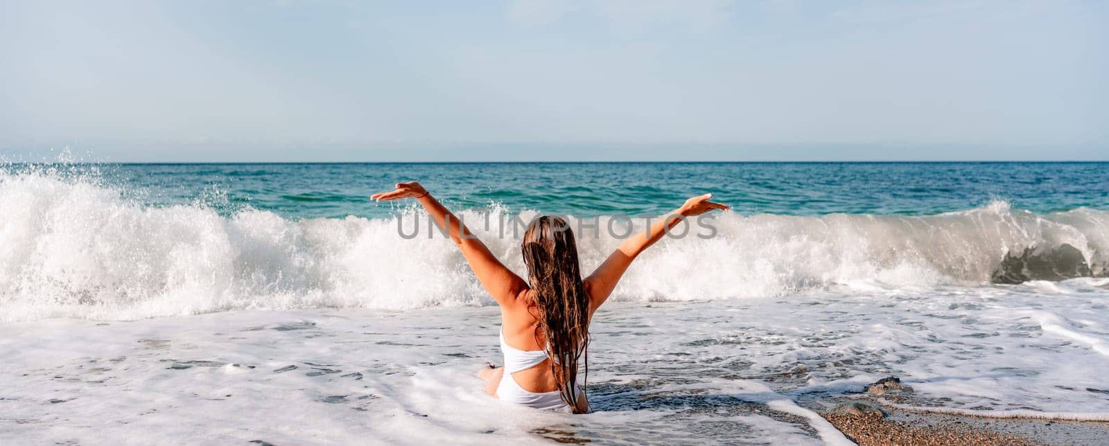 Happy woman in bikini sits on the sea beach. Tanned girl sunbathing on a beautiful shore. Summer vacation or holiday travel concept.