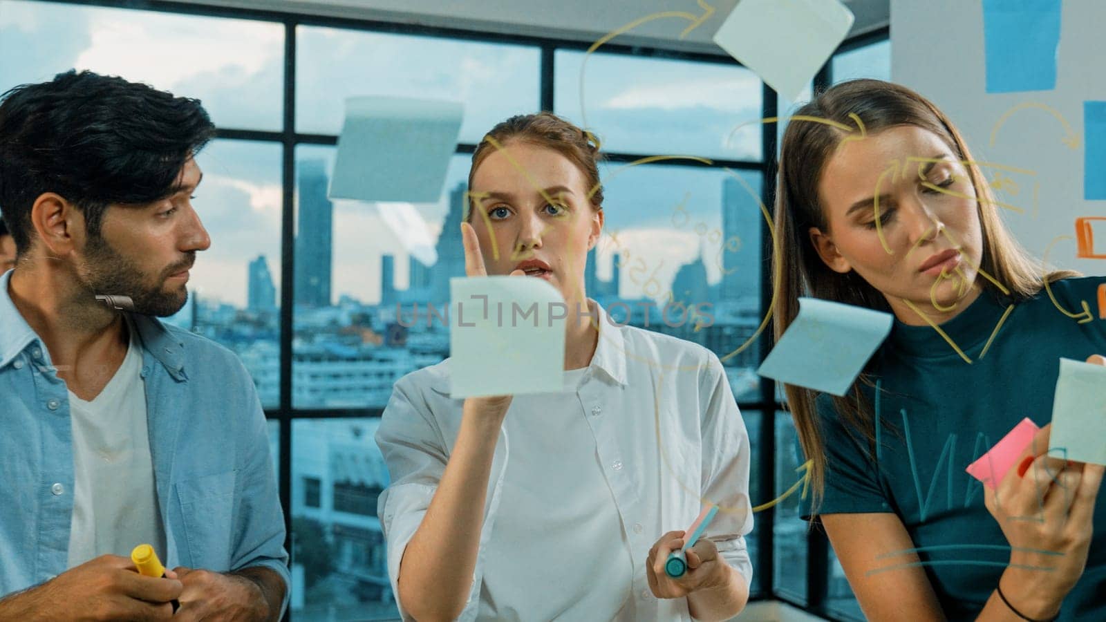 Professional business team brainstorm, sharing, thinking idea while skilled male leader write on sticky notes at glass wall. Skilled manager placed business plan on glass wall at office. Tracery