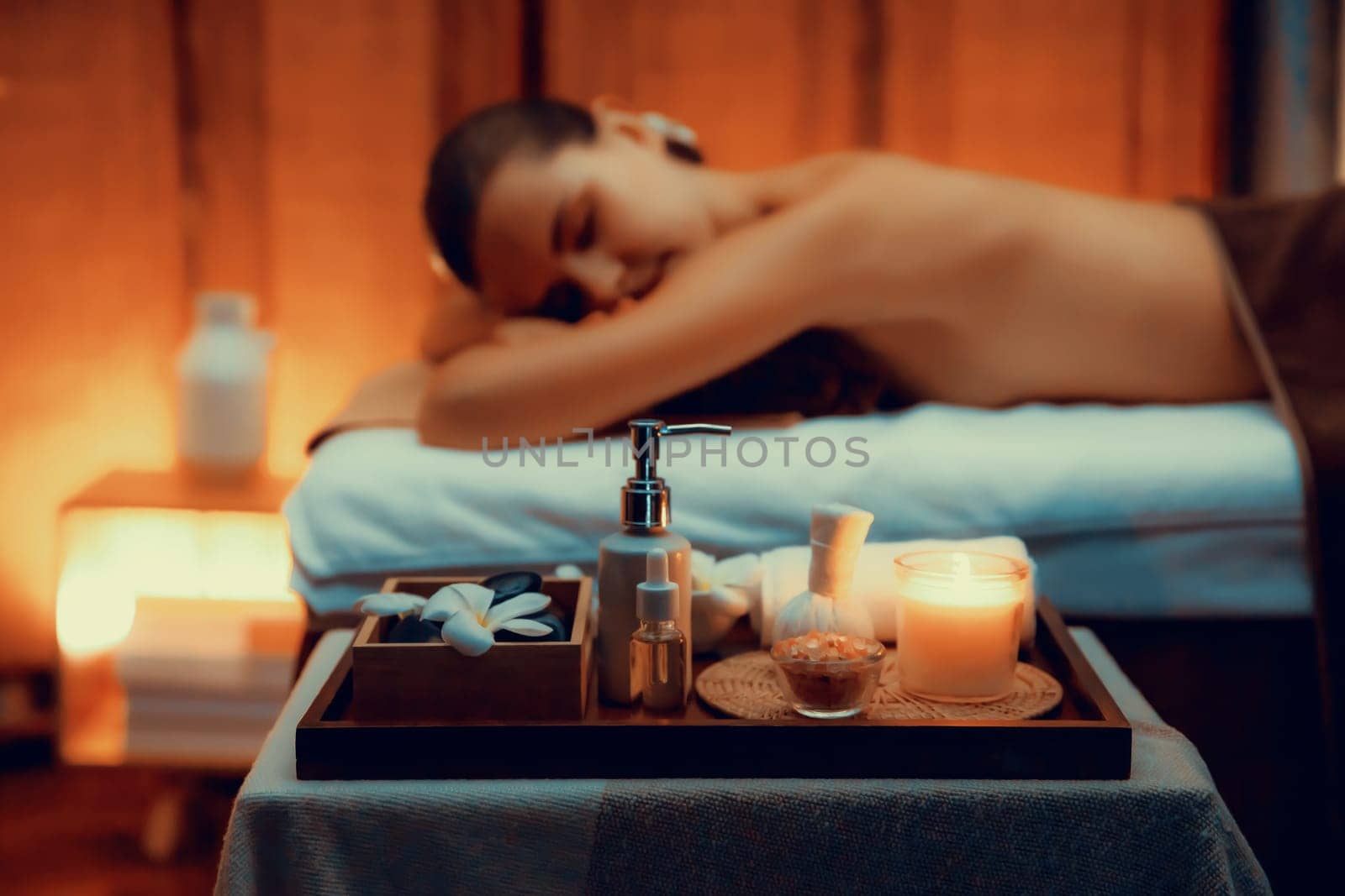 Aromatherapy massage ambiance or spa salon composition setup with focus decor candles and spa accessories on blurred woman enjoying blissful aroma spa massage in resort or hotel background. Quiescent