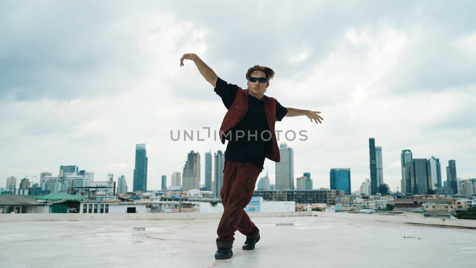 Motion shot of B-boy dance performance by professional street dancer at rooftop with sky scrapper, city view. Attractive asian hipster show energetic footstep. Outdoor sport 2024. Endeavor.