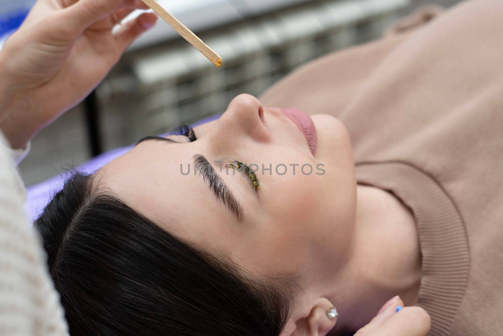 Beauty concept. Eyelash extensions. A beautiful girl lies on a couch in a beauty salon. The master does eyelash extensions. Close-up.