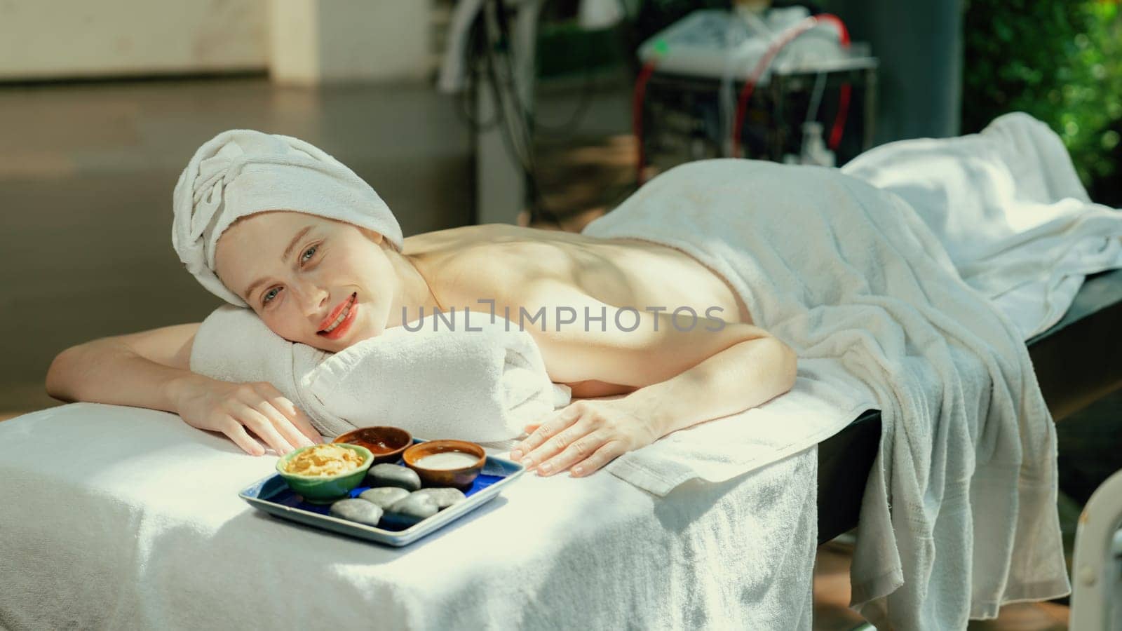 Relaxing beautiful young woman lies on spa bed near ingredients of homemade facial mask while looking at camera surrounded by beauty electrical equipment. Healthy and beauty concept. Tranquility.
