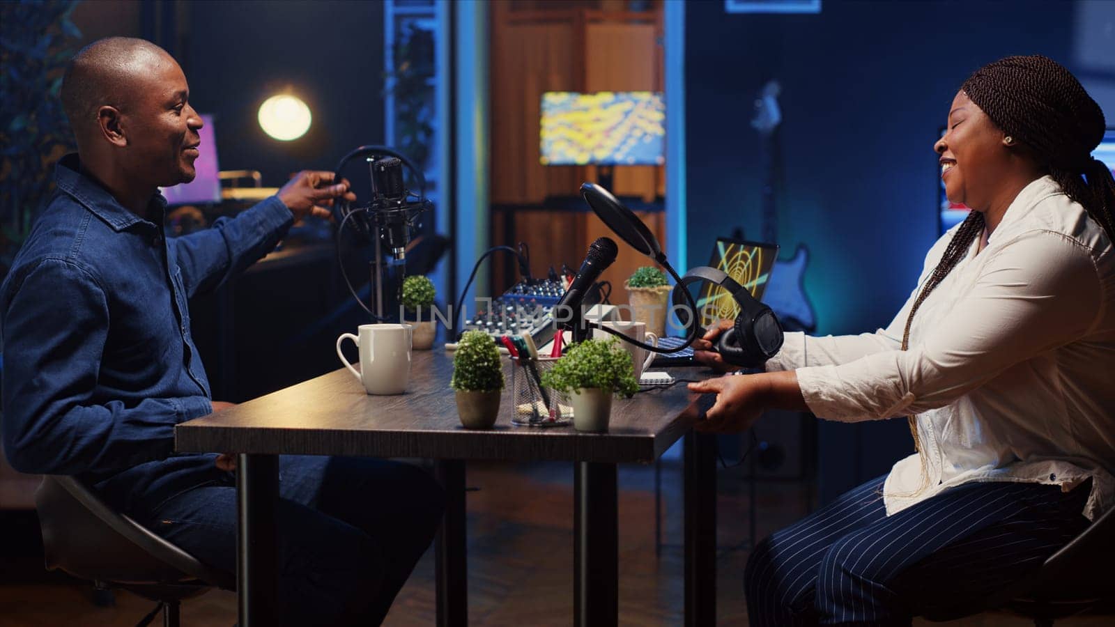 African american man invited to podcast entering studio with host, ready to participate in entertaining discussion. Smiling guest sitting down and putting on headphones for online comedy show