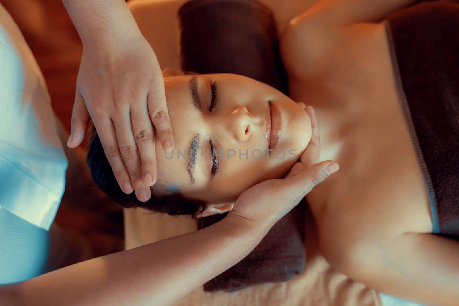 Caucasian woman enjoying relaxing anti-stress head massage and pampering facial beauty skin recreation leisure in warm candle lighting ambient salon spa in luxury resort or hotel. Quiescent