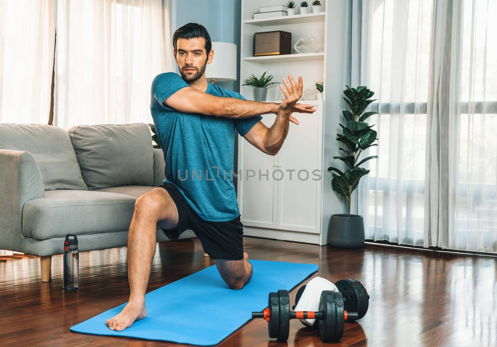 Athletic and sporty man doing warmup and stretching before home body workout exercise session for fit physique and healthy sport lifestyle at home. Gaiety home exercise workout training concept.