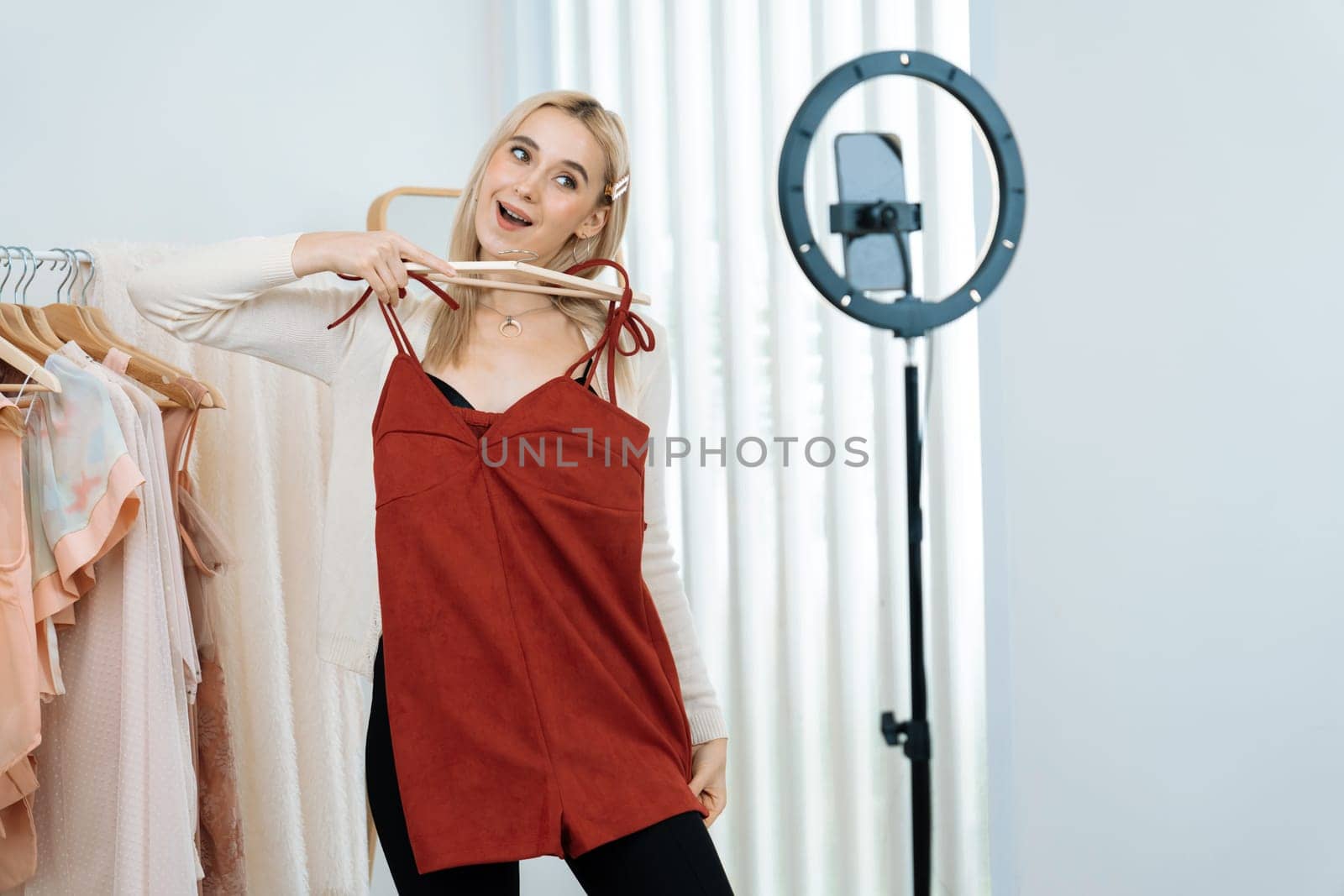 Young social medial content creator woman make fashion video. Blogger smiles to camera and light ring while making persuasive online clothing sell vlog to audience or follower. Blithe