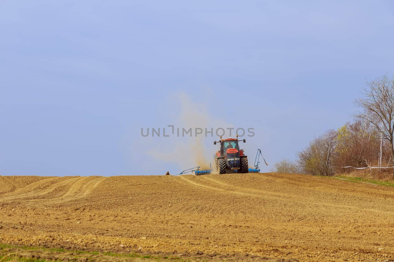 The tractor sows the field with grain, the dust has risen to the top. by Yaroslav