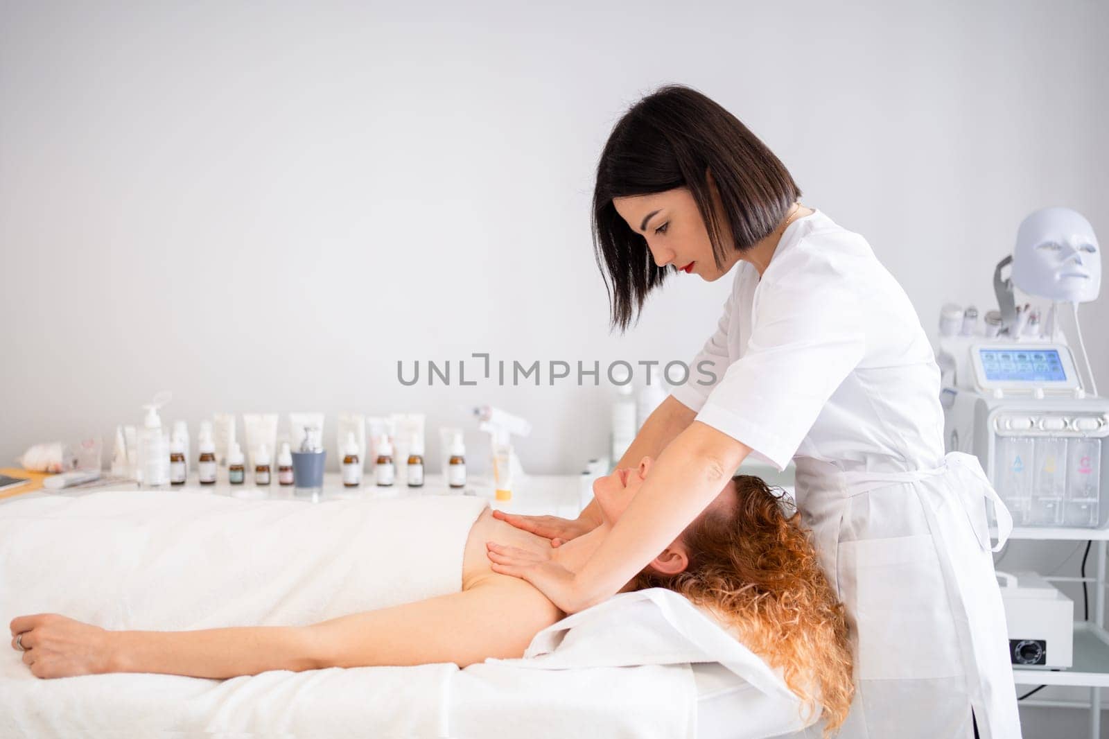 Side view of masseuse massaging woman's head, shoulders, and neck in beauty center. Beauty Treatments. Body care, skin care, wellness, and wellbeing concepts.