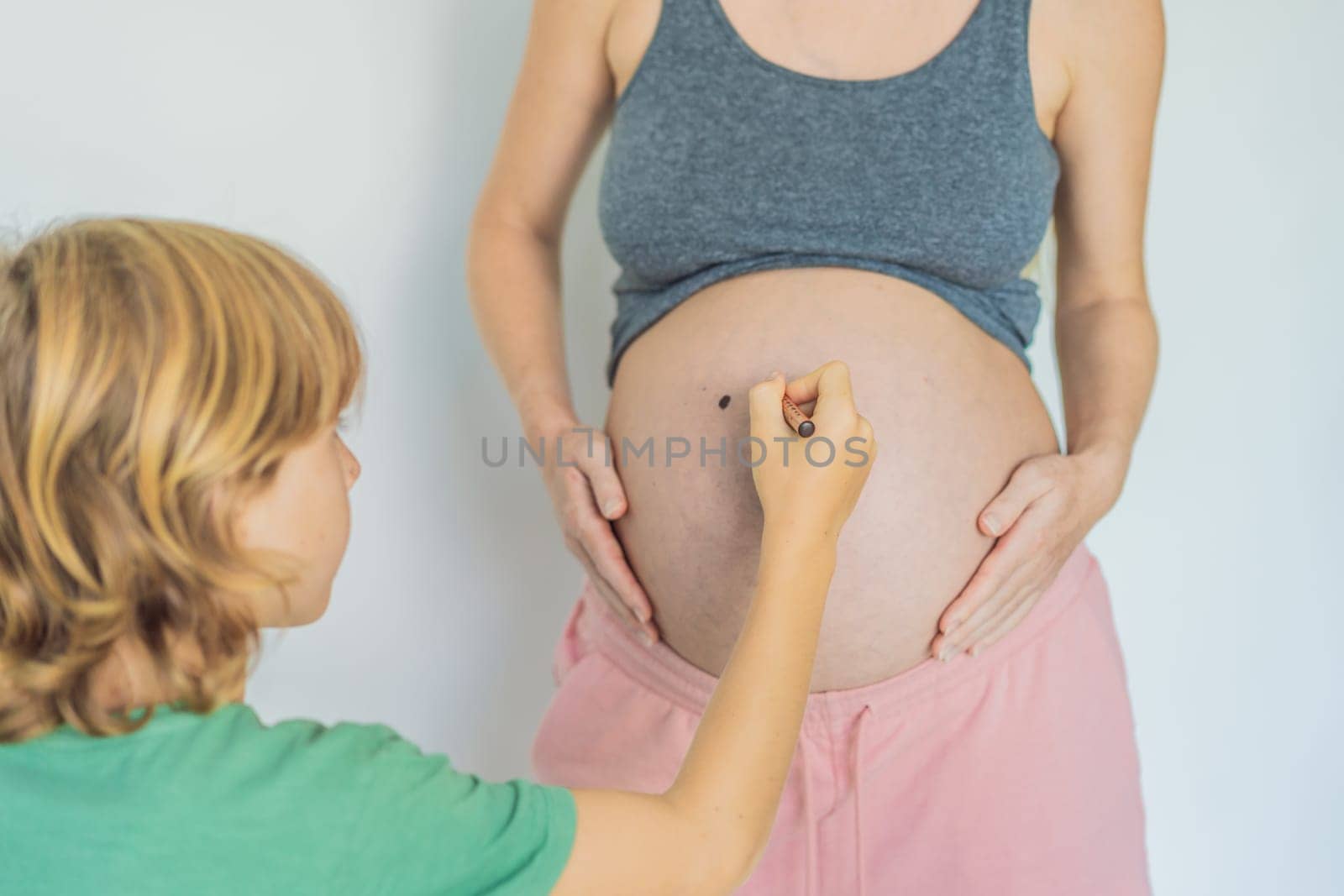 Adorable moment as a son adds a touch of joy to his mother's pregnancy, playfully drawing a funny face on her baby bump, creating cherished memories by galitskaya