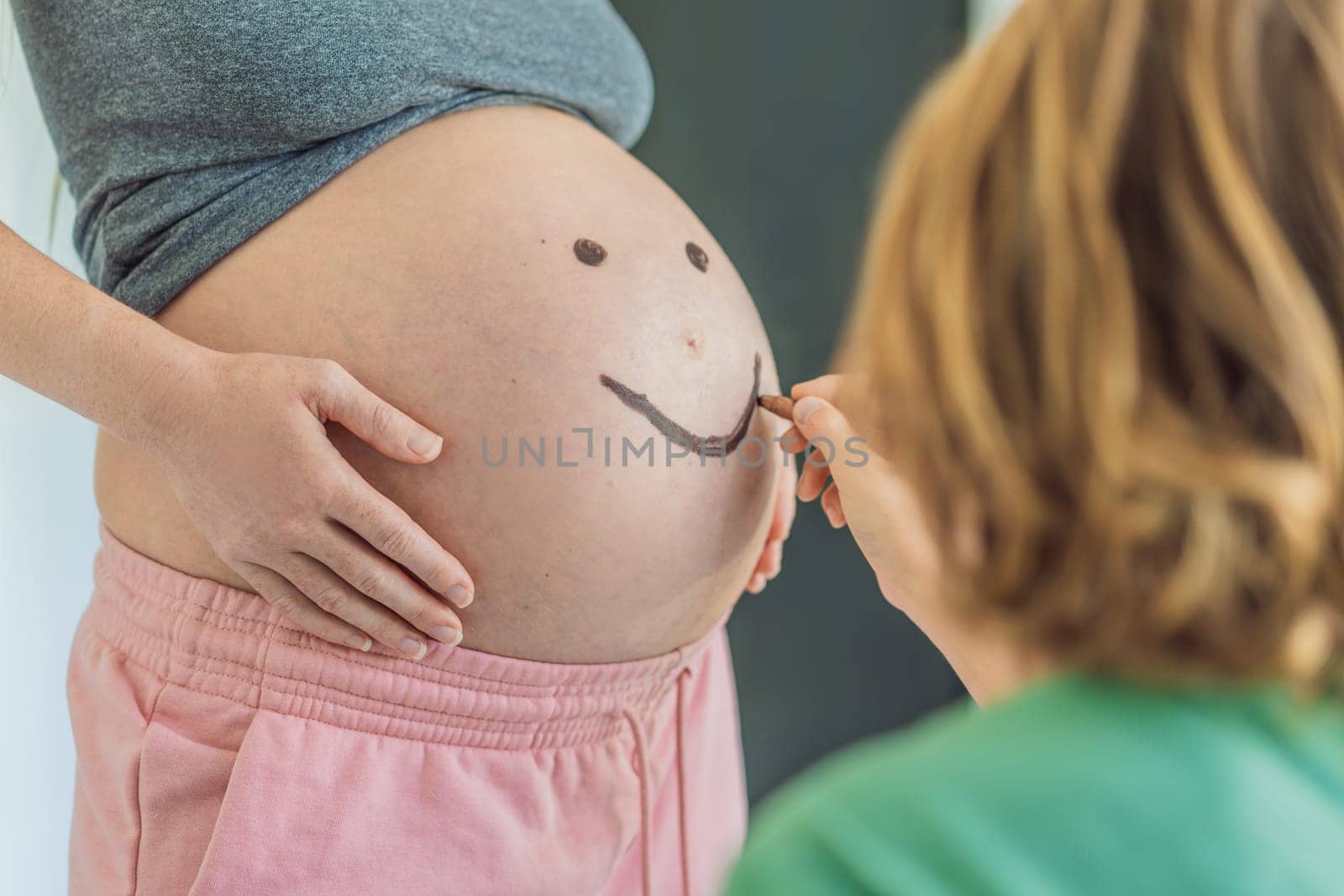 Adorable moment as a son adds a touch of joy to his mother's pregnancy, playfully drawing a funny face on her baby bump, creating cherished memories by galitskaya