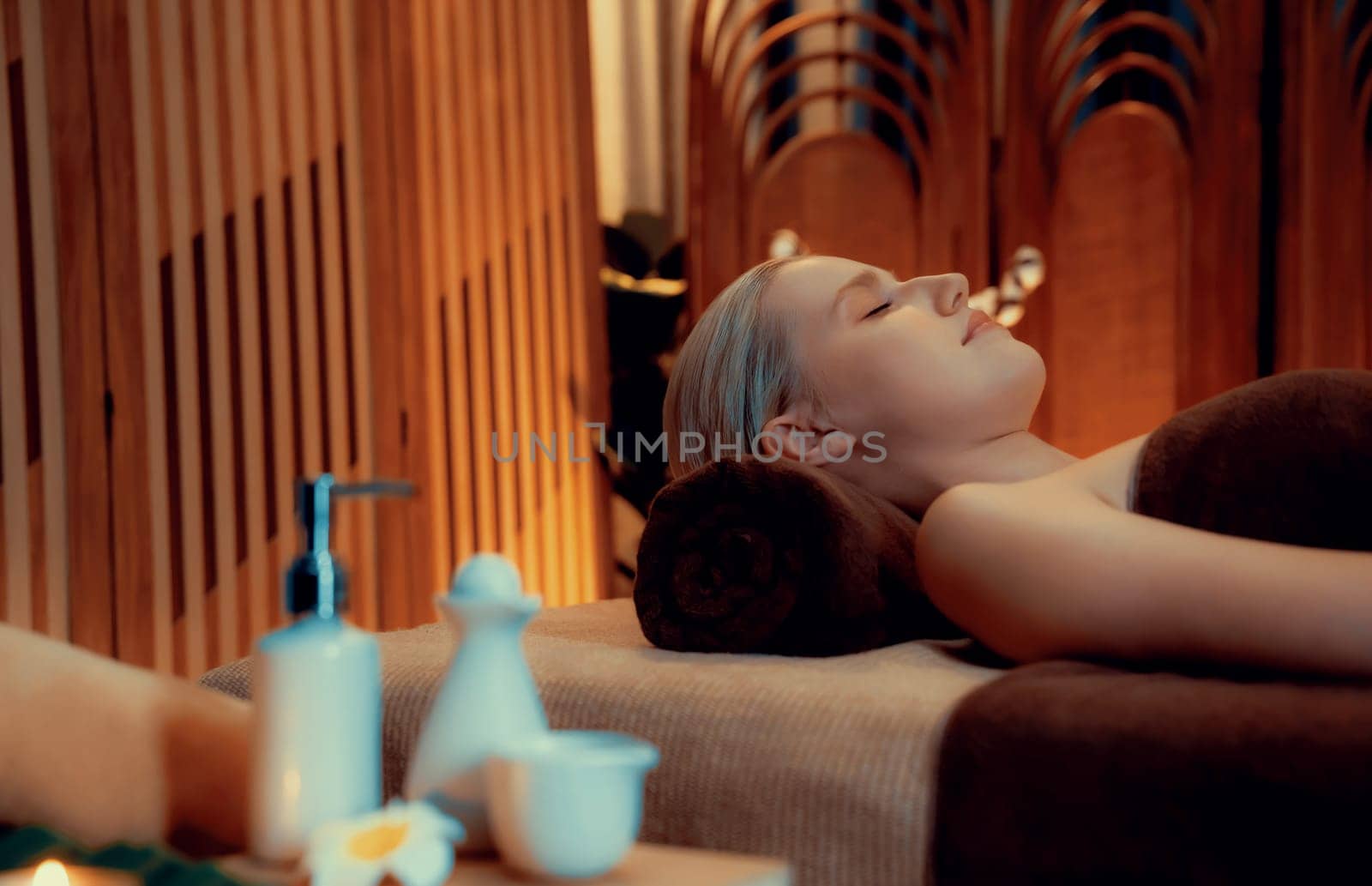 Caucasian woman customer enjoying relaxing anti-stress spa massage and pampering with beauty skin recreation leisure in warm candle lighting ambient salon spa at luxury resort or hotel. Quiescent