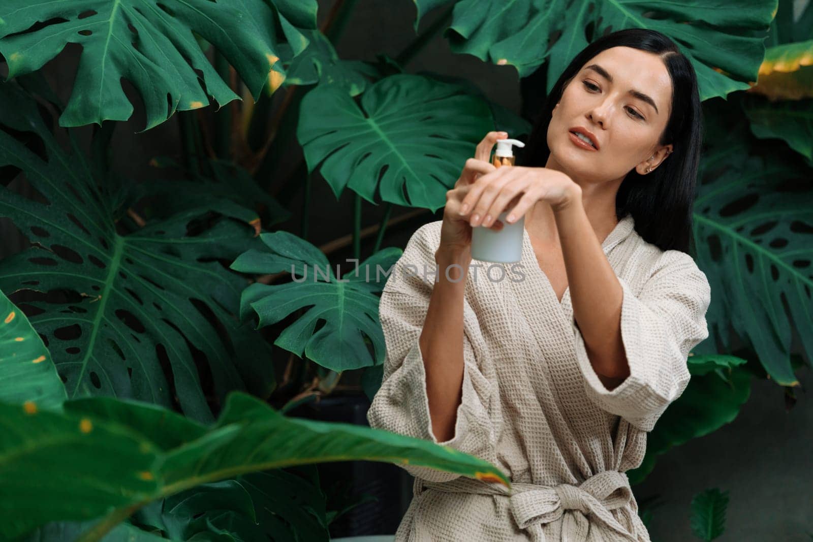 Tropical and exotic spa garden with bathtub in modern hotel or resort with woman in bathrobe holding beauty skincare product while enjoying leisure lush with greenery foliage background. Blithe