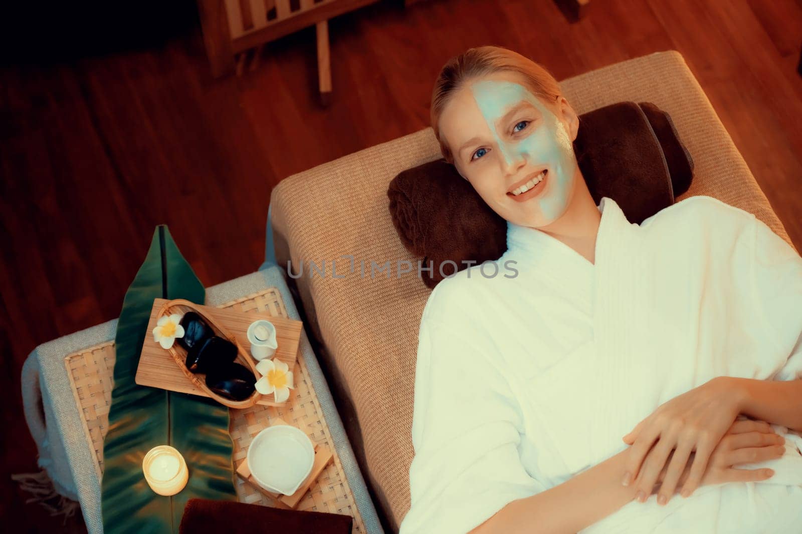 Serene ambiance of spa salon, woman customer smiling and rejuvenating with luxurious face cream massage with warm lighting candle. Facial skin treatment and beauty care concept. Quiescent