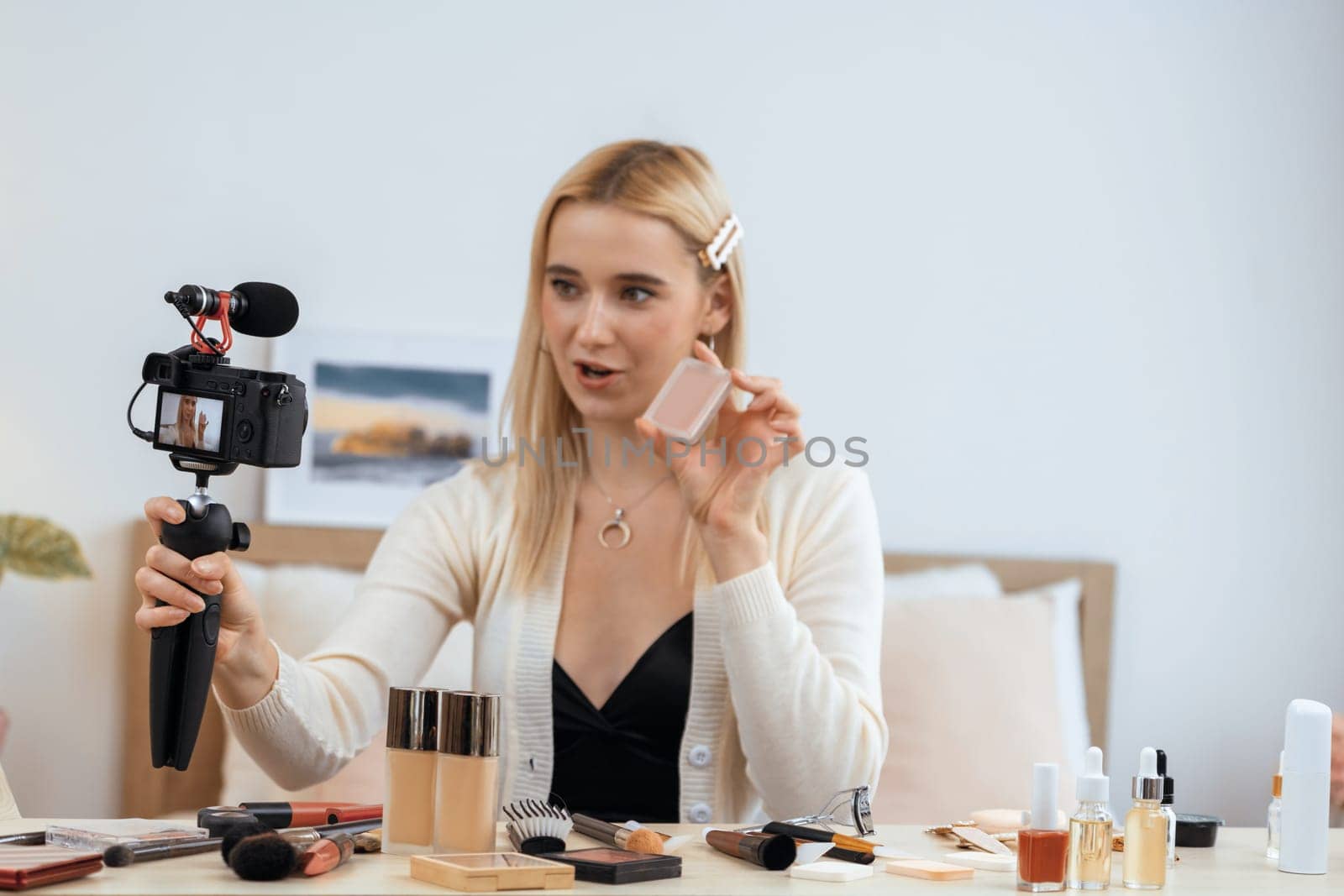 Young woman making beauty and cosmetic tutorial video content for social media. Beauty blogger smiles to camera while showing how to beauty care to audience or followers. Blithe