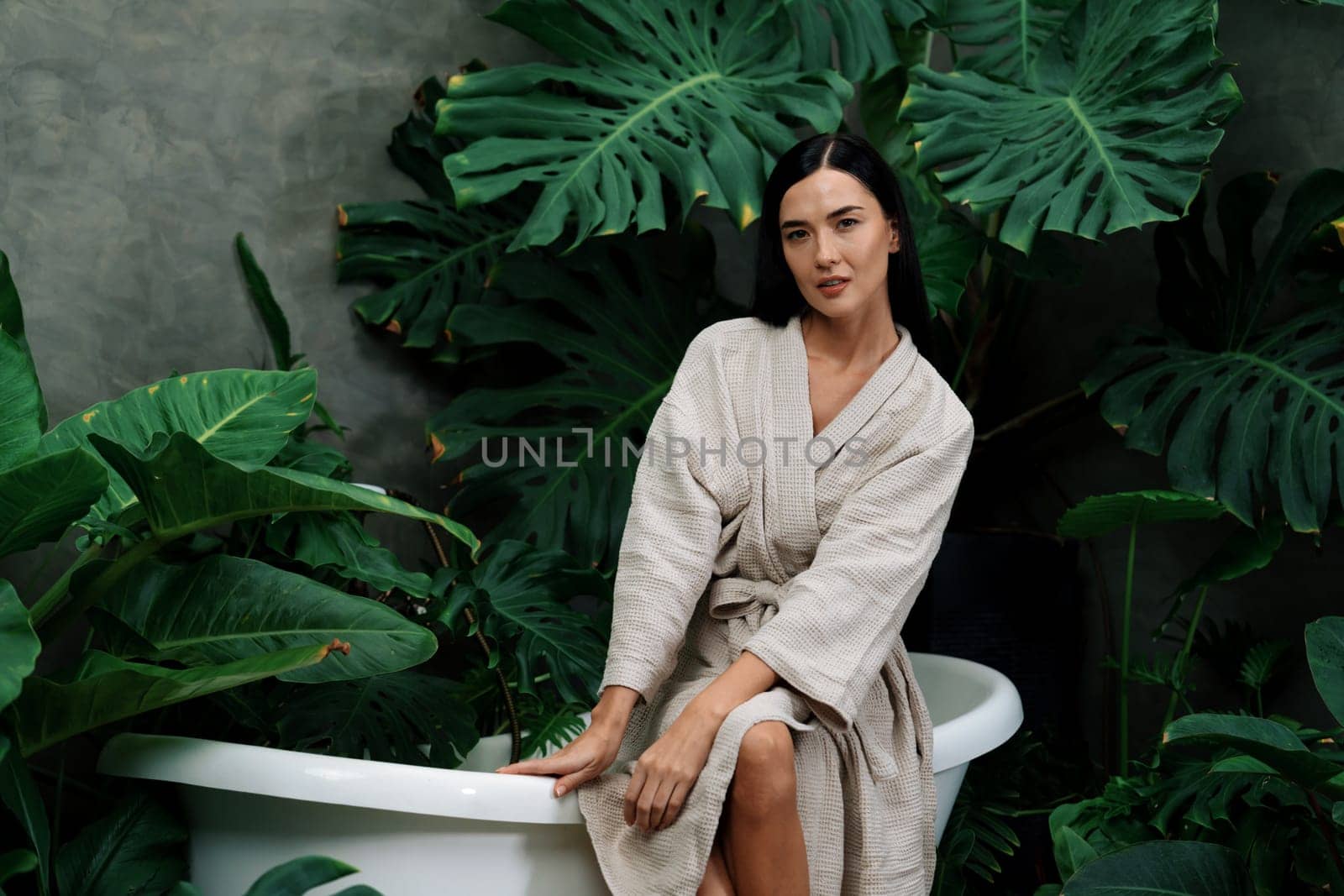 Tropical and exotic spa garden with bathtub in modern hotel or resort with young woman in bathrobe enjoying leisure and wellness lifestyle surrounded by lush greenery foliage background. Blithe