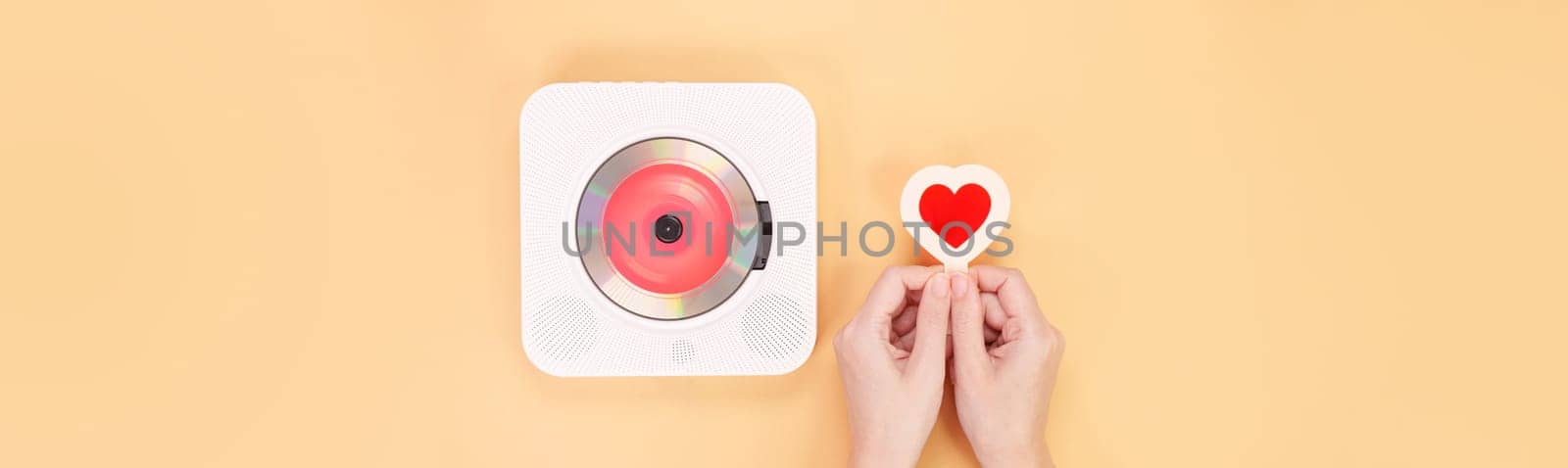 Hands holding heart shape red gift card next to white cd player with red disc on yellow background. Love music, Valentine day, Greeting, retro Love song, space for text. by JuliaDorian