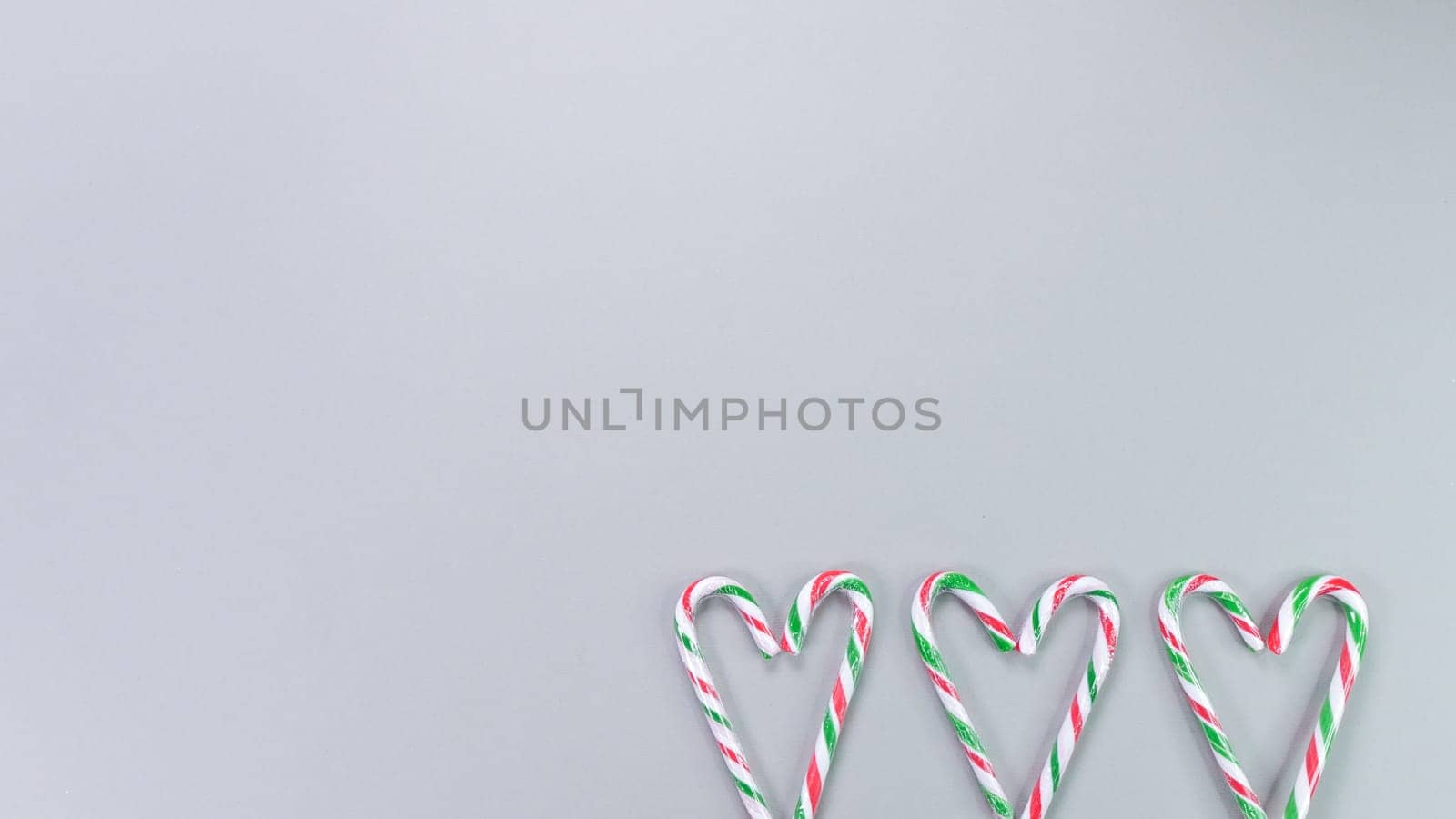 Red, green and white candy canes in the shape of heart on grey background. Valentine's Day concept. Greeting card with copy space for your text or advertising, flat lay