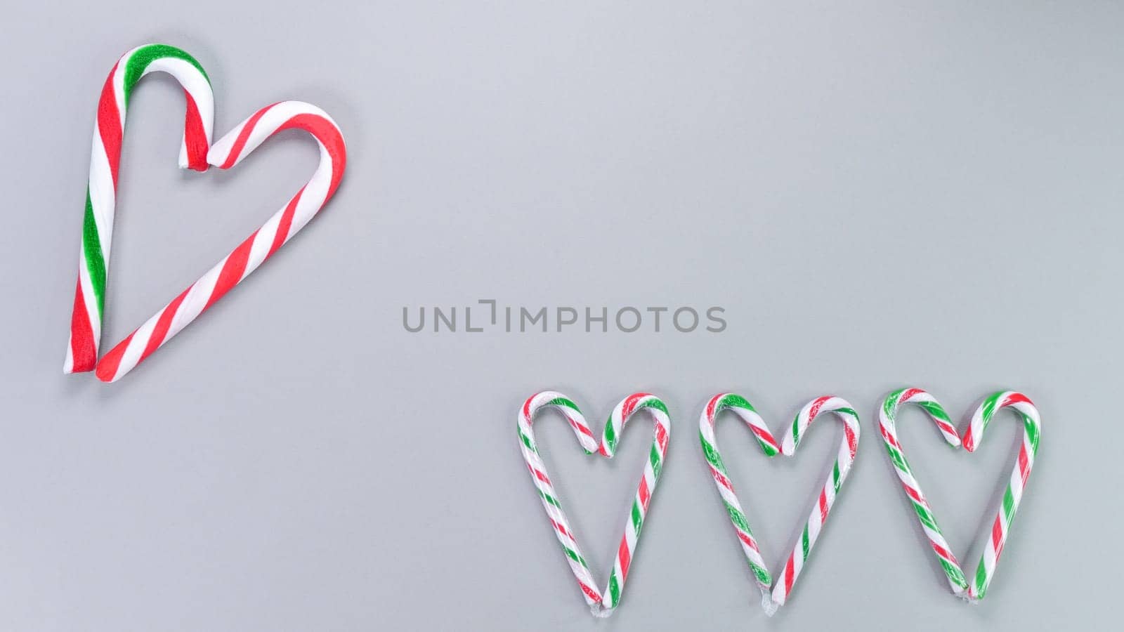 Red, green and white candy canes in the shape of heart on grey background. Valentine's Day concept. Greeting card with copy space for your text or advertising, flat lay. by JuliaDorian