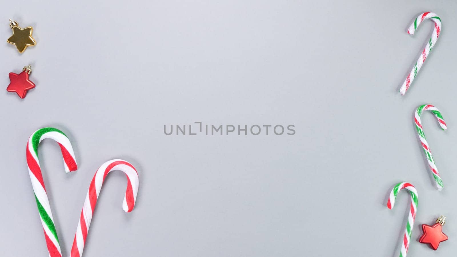 Christmas candy cane, golden and red stars, small and big candies on grey background. Christmas composition. Top view, flat lay.