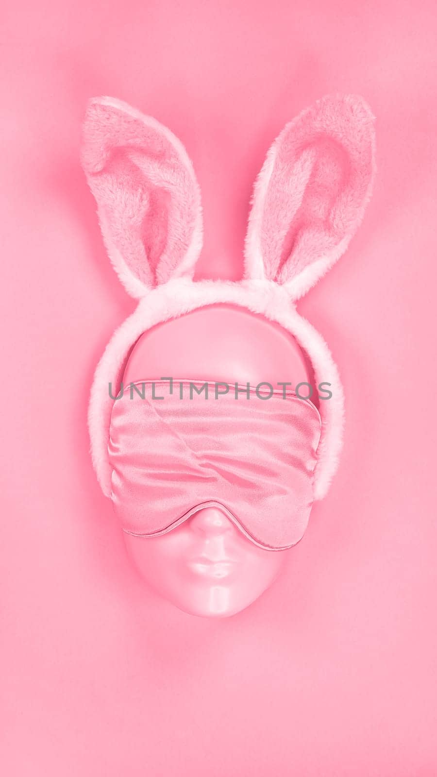 Pink sleeping eye mask on mannequin face with fluffy Easter bunny ears. Image is toned in Viva Magenta color of year 2023. sleeping disorder. Holidays, Head accessory. Plastic face