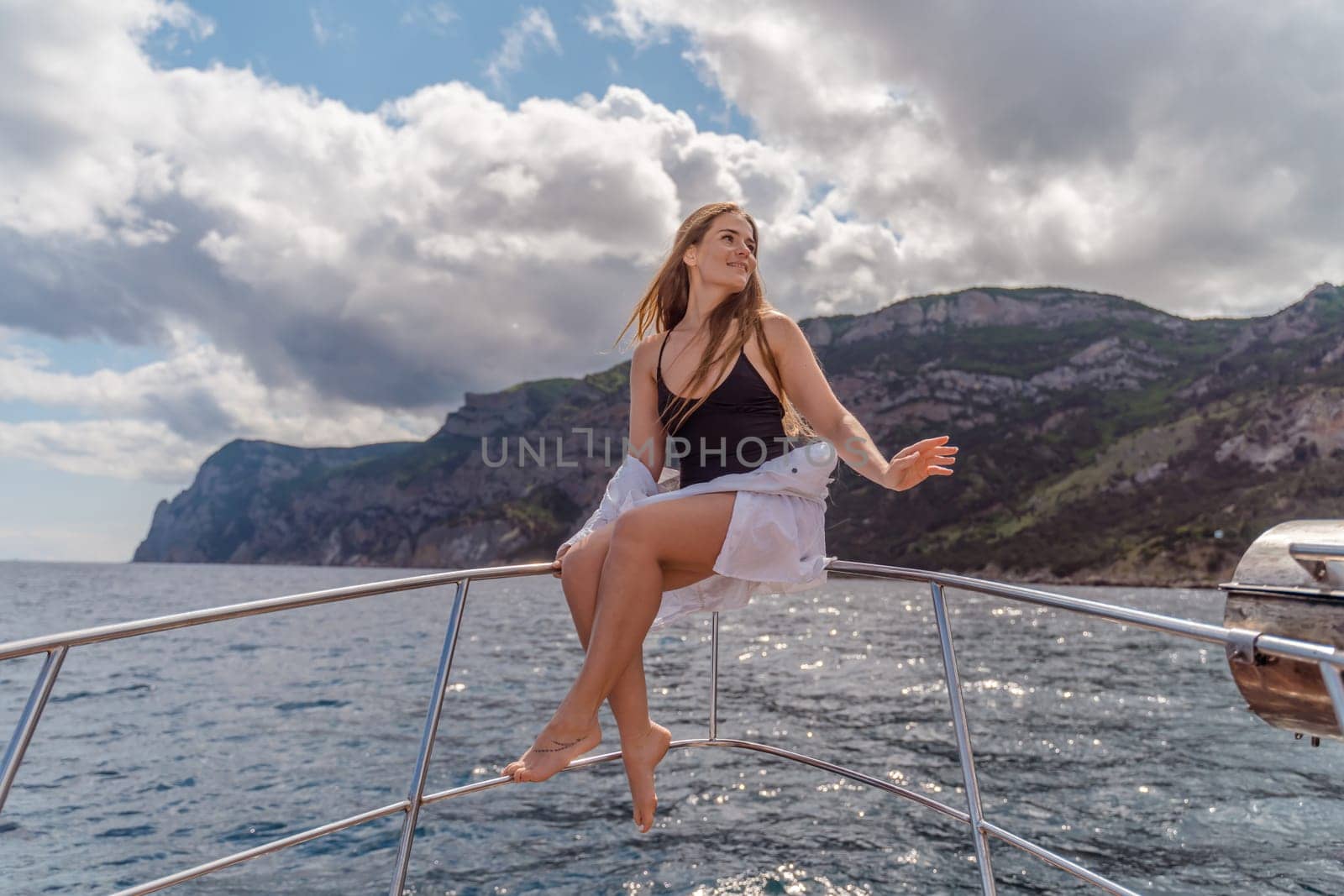 Woman on a yacht. Happy model in a swimsuit posing on a yacht against a blue sky with clouds and mountains.