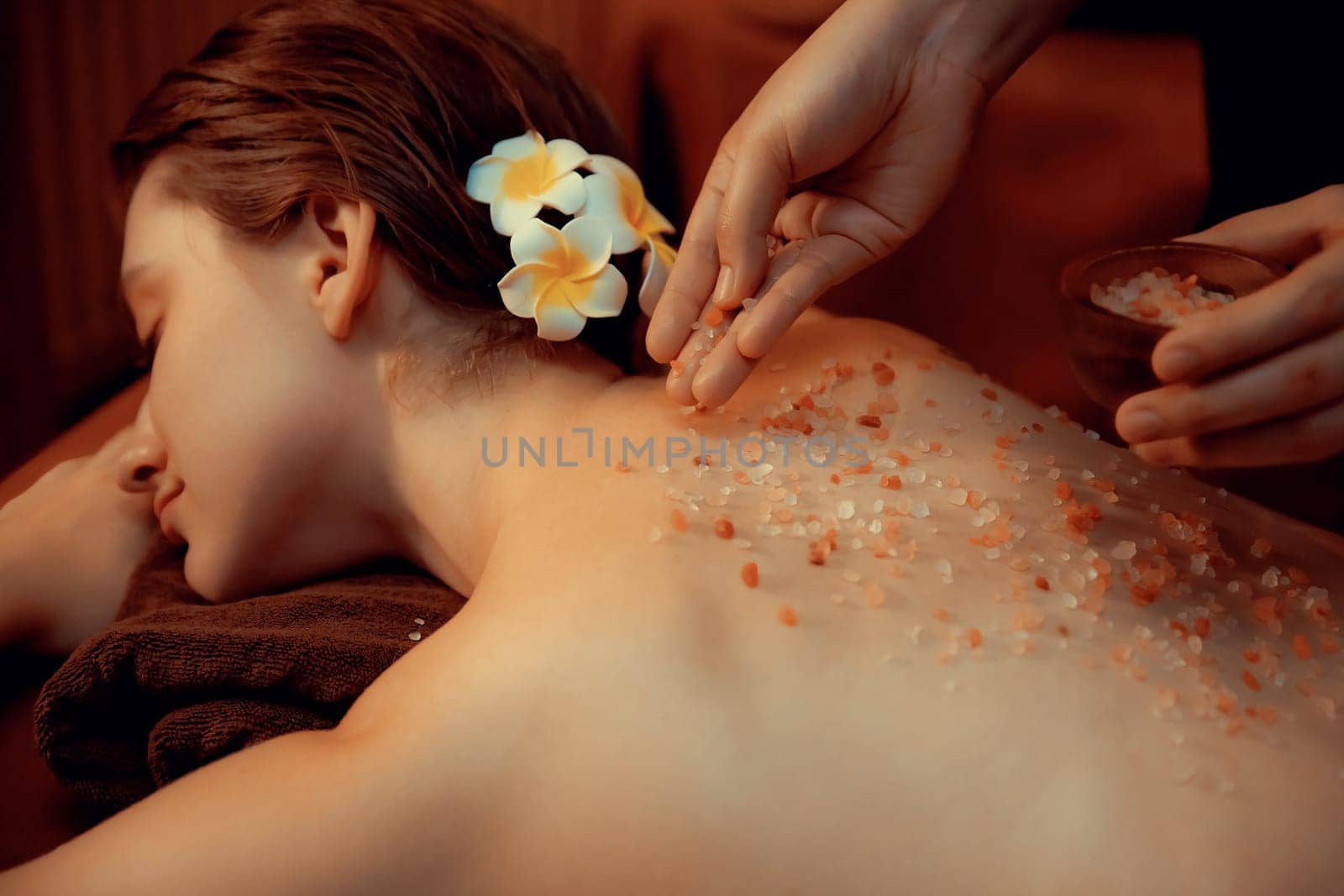 Woman customer having exfoliation treatment in luxury spa salon with warmth candle light ambient. Salt scrub beauty treatment in Health spa body scrub. Quiescent