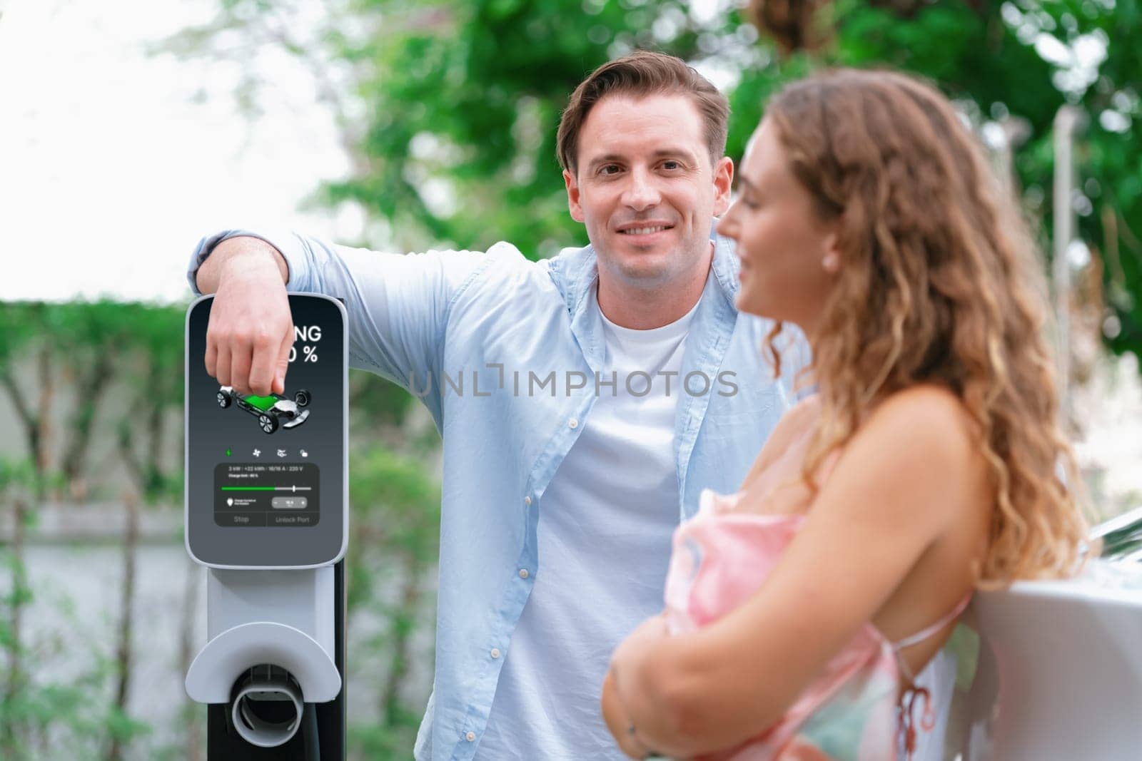 Happy and lovely couple with eco-friendly conscious recharging electric vehicle from EV charging station. EV car technology utilized as alternative transportation for future sustainability. Synchronos