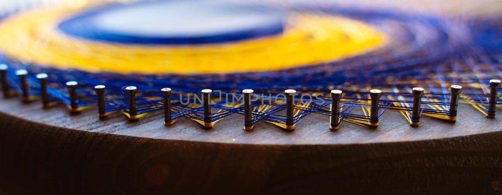 Colored thread mandala on a wooden board with nails. Mandala Moon Harmony Sun esotericism and psychology pictures from yellow and blue silk threads