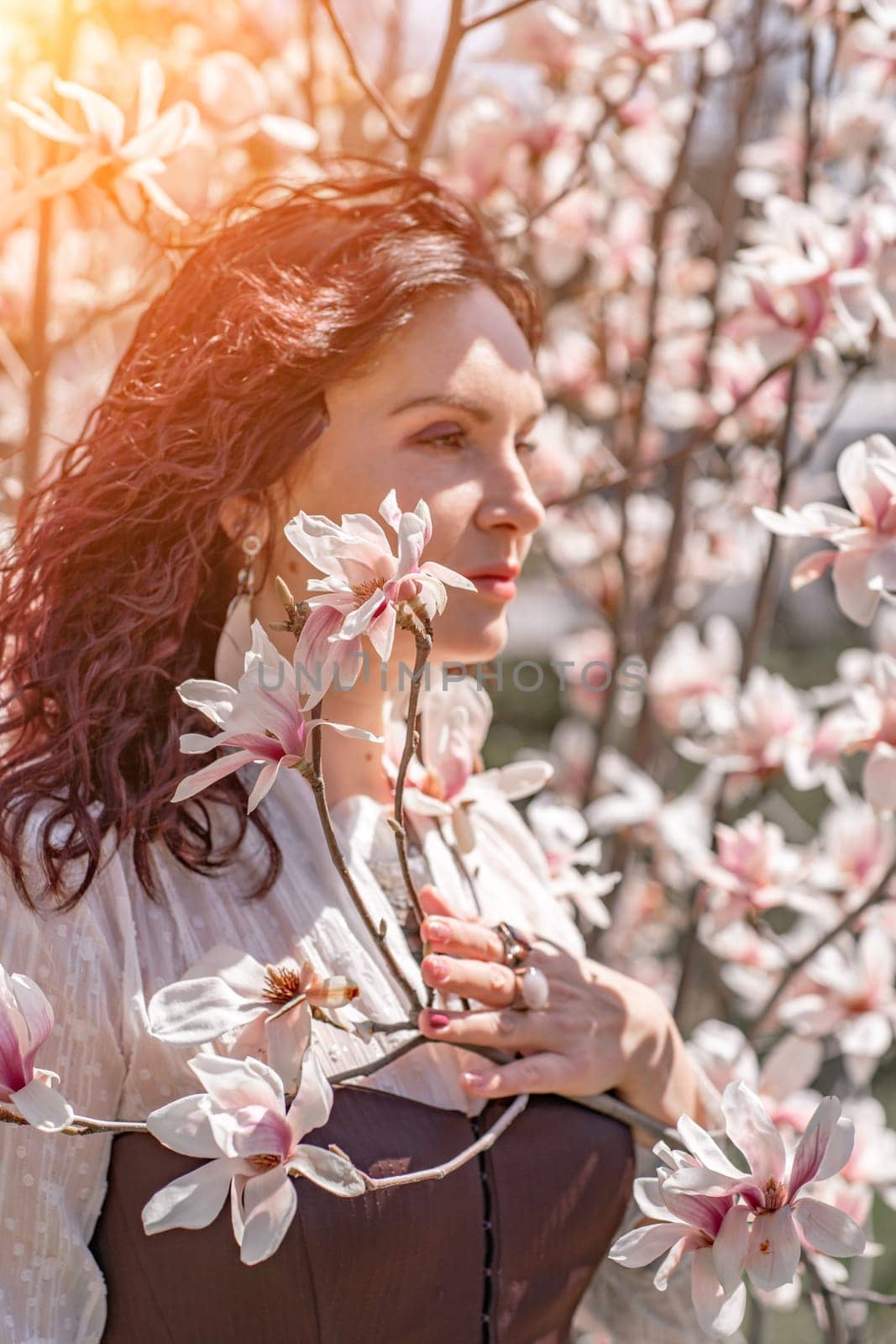 Magnolia park woman. Stylish woman in a hat stands near the magnolia bush in the park. Dressed in white corset pants and posing for the camera. by Matiunina