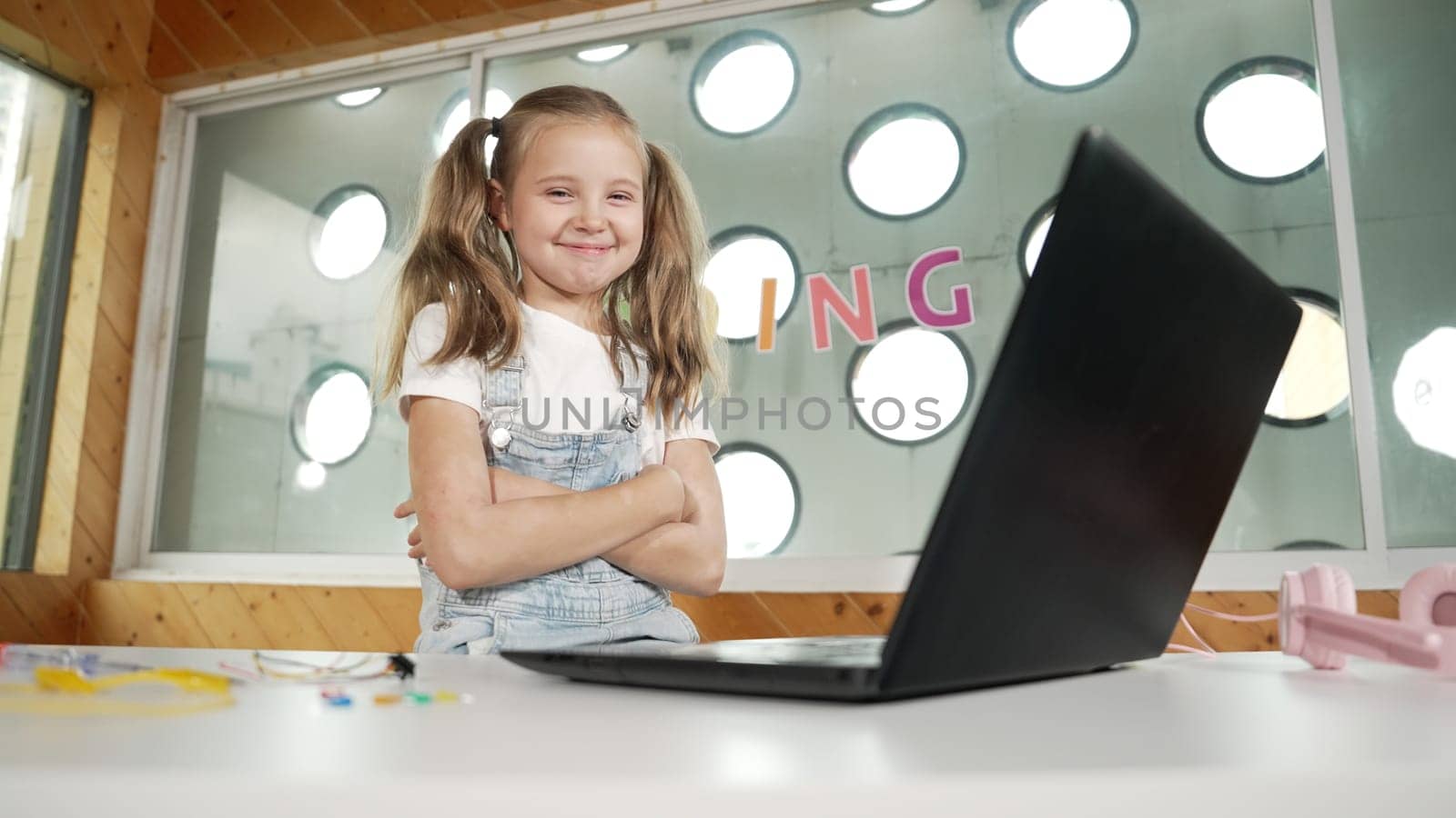 Girl using laptop programing software while looking at camera with arm folded with confident to celebrate successful project. Pretty child coding system while crossing arms in Stem class. Erudition.