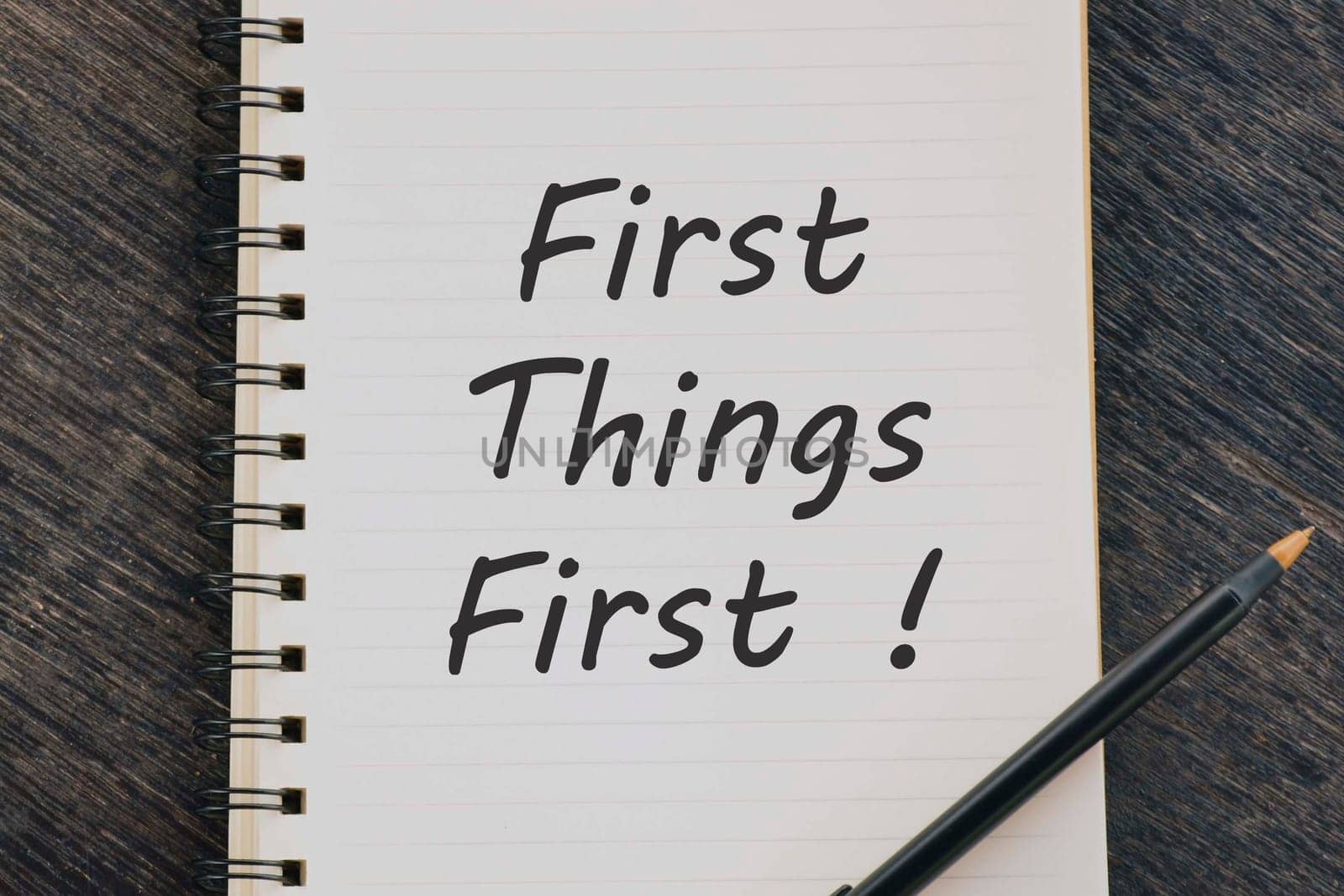 First Things First text on notepad with pen on wooden desk.