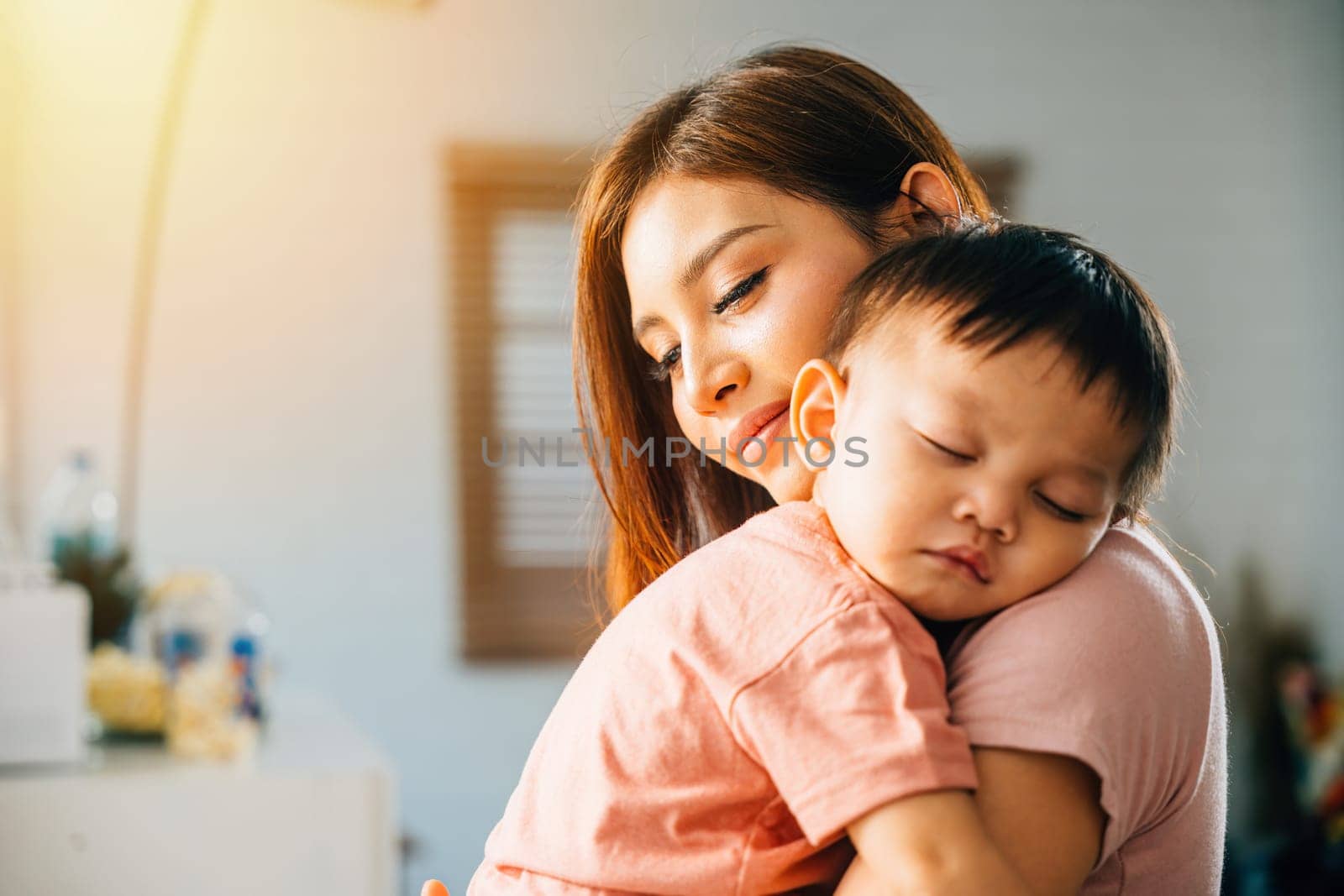 In the comfort of their home an Asian mom hugs her tiny slumbering infant celebrating a heartwarming family moment filled with joy bonding and the carefree moments of childhood.