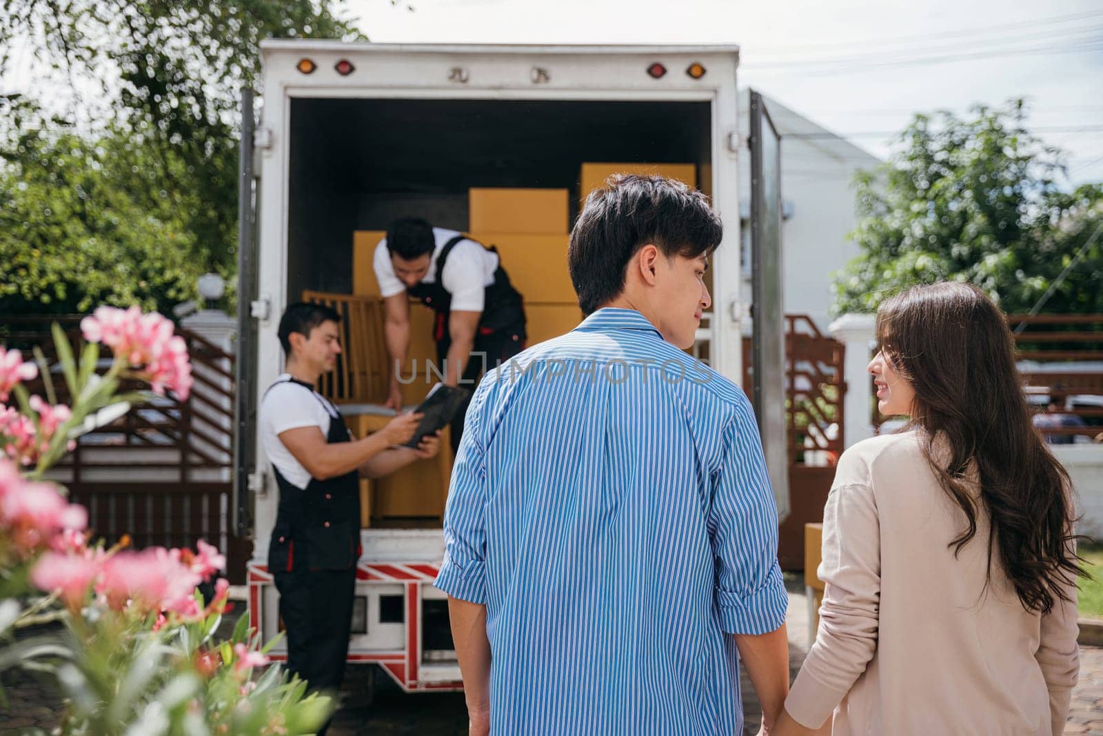 Assisted by a professional delivery team a couple transitions to their new home. Together they unload and lift cardboard boxes ensuring an organized and efficient move. Moving Day Concept by Sorapop