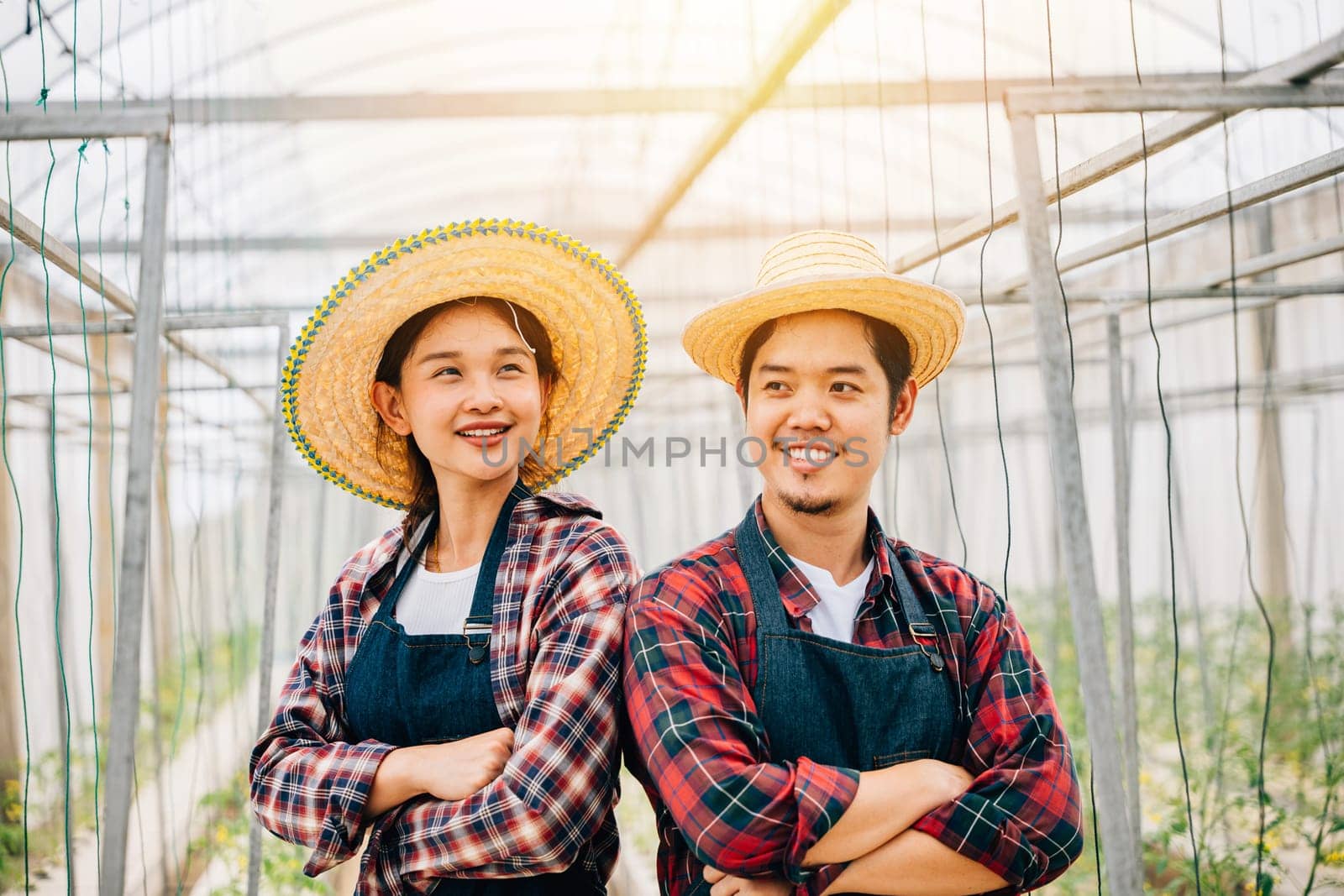 Happy Asian couple farmers working in tomato hydroponic farm. Smiling man and woman crossed arms with vegetable success. Portrait of confident husband and wife in greenhouse. Quality farming.