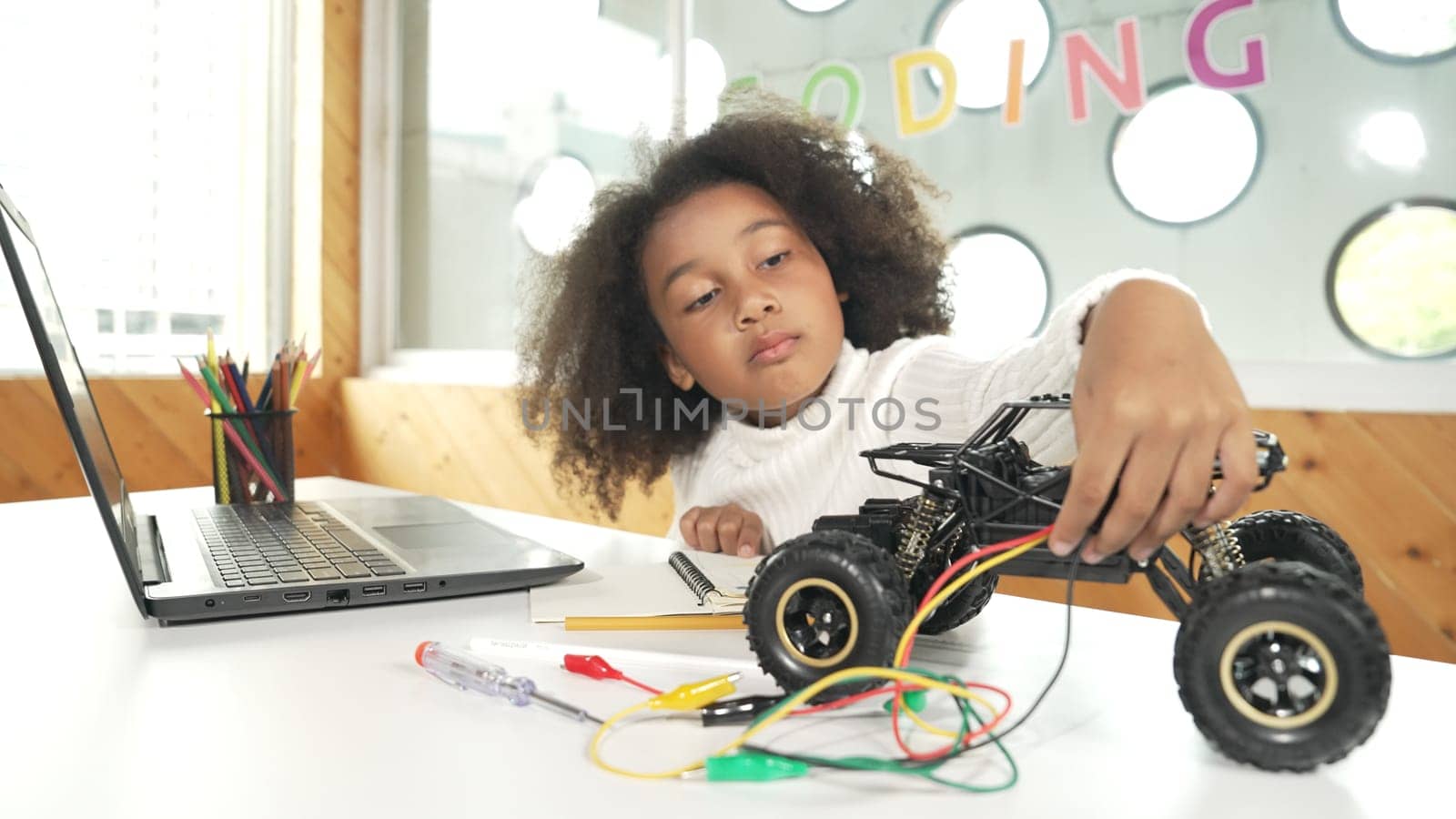 Smart african girl build robotic car while using wires while using laptop setting or writing prompt code. Skilled female student working on computer in STEM technology online classroom. Erudition.