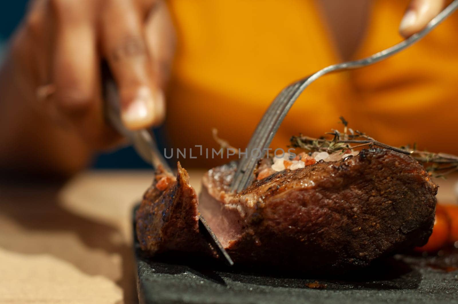 A close-up shot capturing the moment a person slices into a juicy, herb-topped steak on a hot stone plate, indicating a mealtime setting.