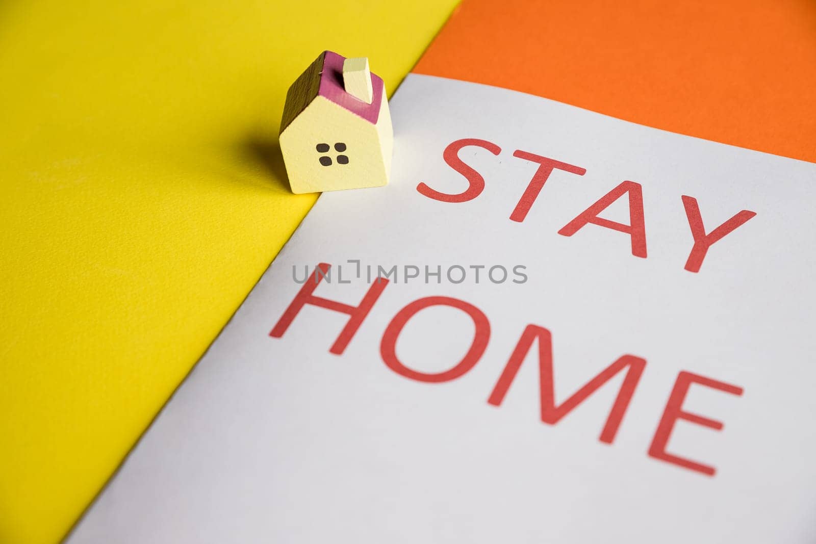 Small wooden toy house on white pastel background with words stay at home.