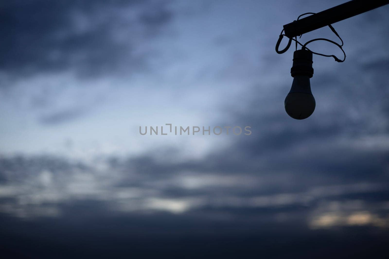 An image of an unlit light bulb against a  cloudy sky.