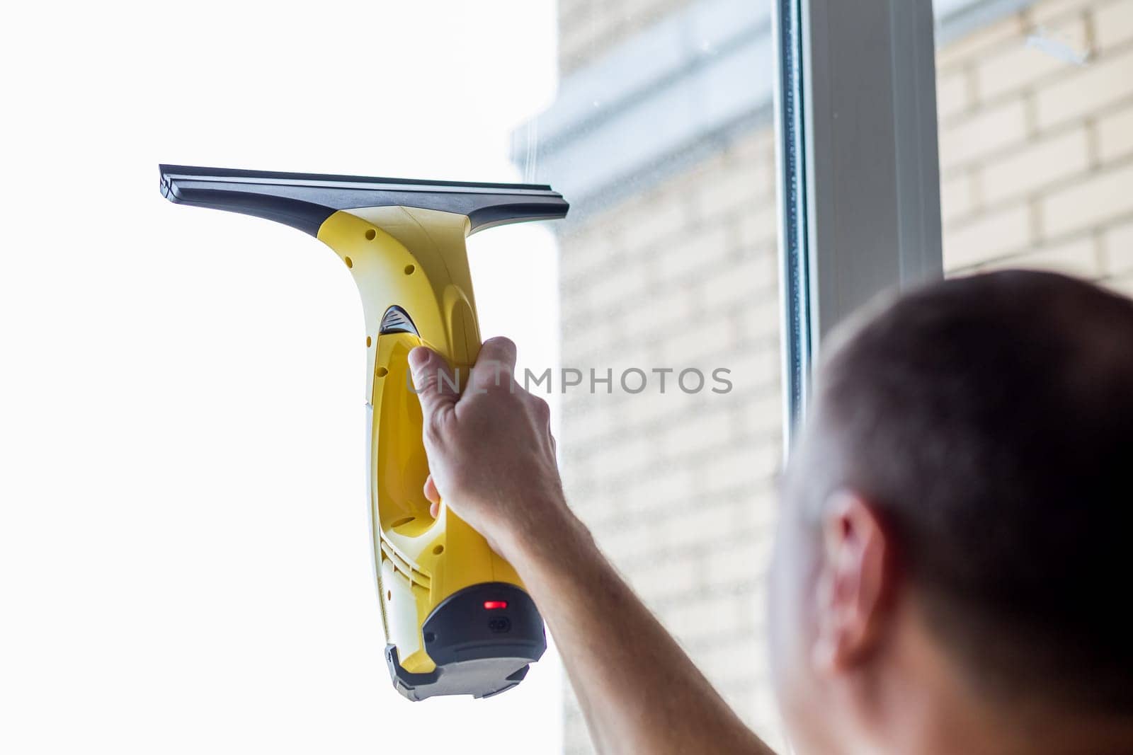 Cleaning windows with vacuum cleaner.worker cleaning glass window of modern building.Men hand with with portable professional electric vacuum cleaner. by YuliaYaspe1979