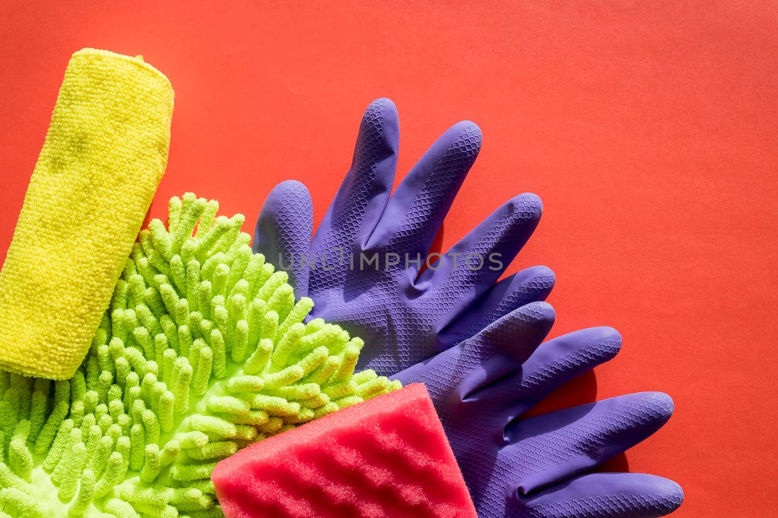Colorful cleaning set for different surfaces in kitchen, rooms. Copy space for text or logo on red background. Cleaning service concept. Early spring regular clean up.Sponge and microfiber rags, protective gloves by YuliaYaspe1979