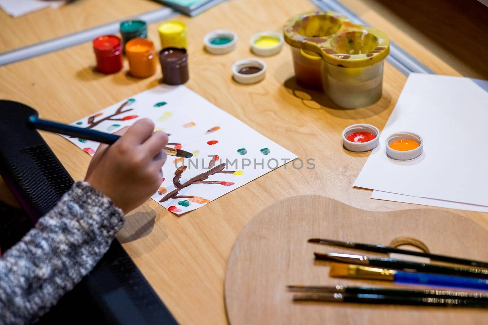 Kid hands painting at the table with gouache,art supplies, selective focus.Learning painting concept, paint brush and box with watercolors on wooden table with splashes, creative art workplace for children kids. by YuliaYaspe1979