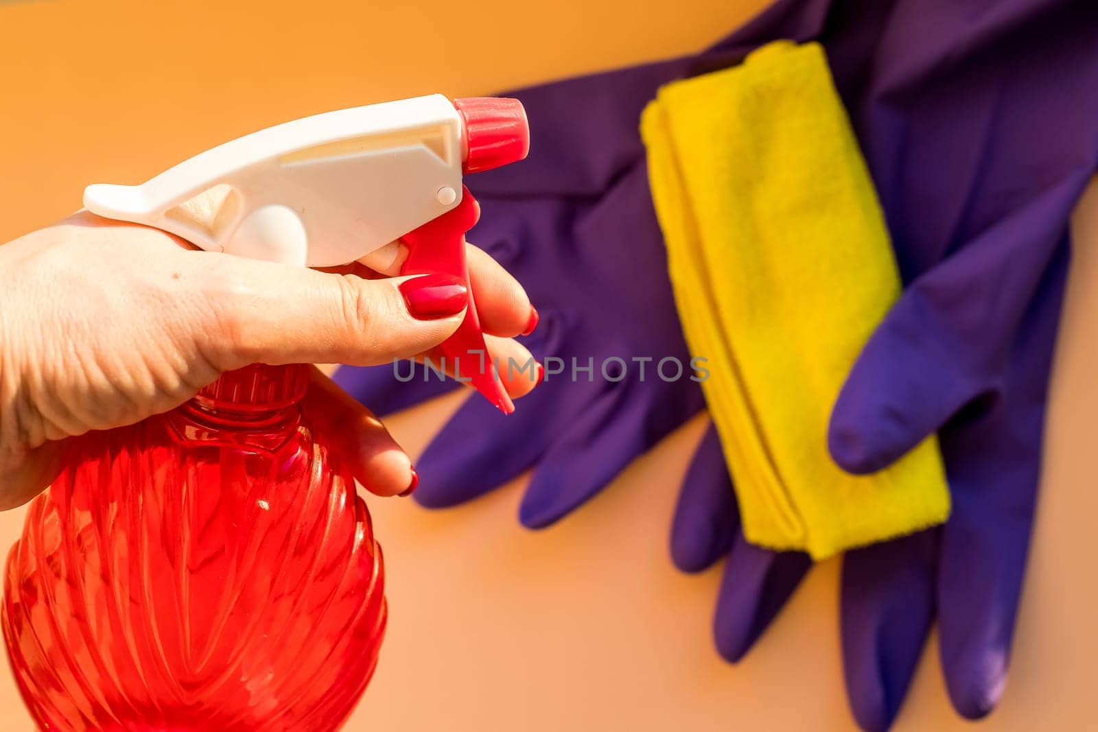 Employee hand holding spray bottle.Cleaning equipment - gloves, sponge and rags on pastel background. Purity concept.purple rubber glove with microfiber cloth.Cleaning items by YuliaYaspe1979